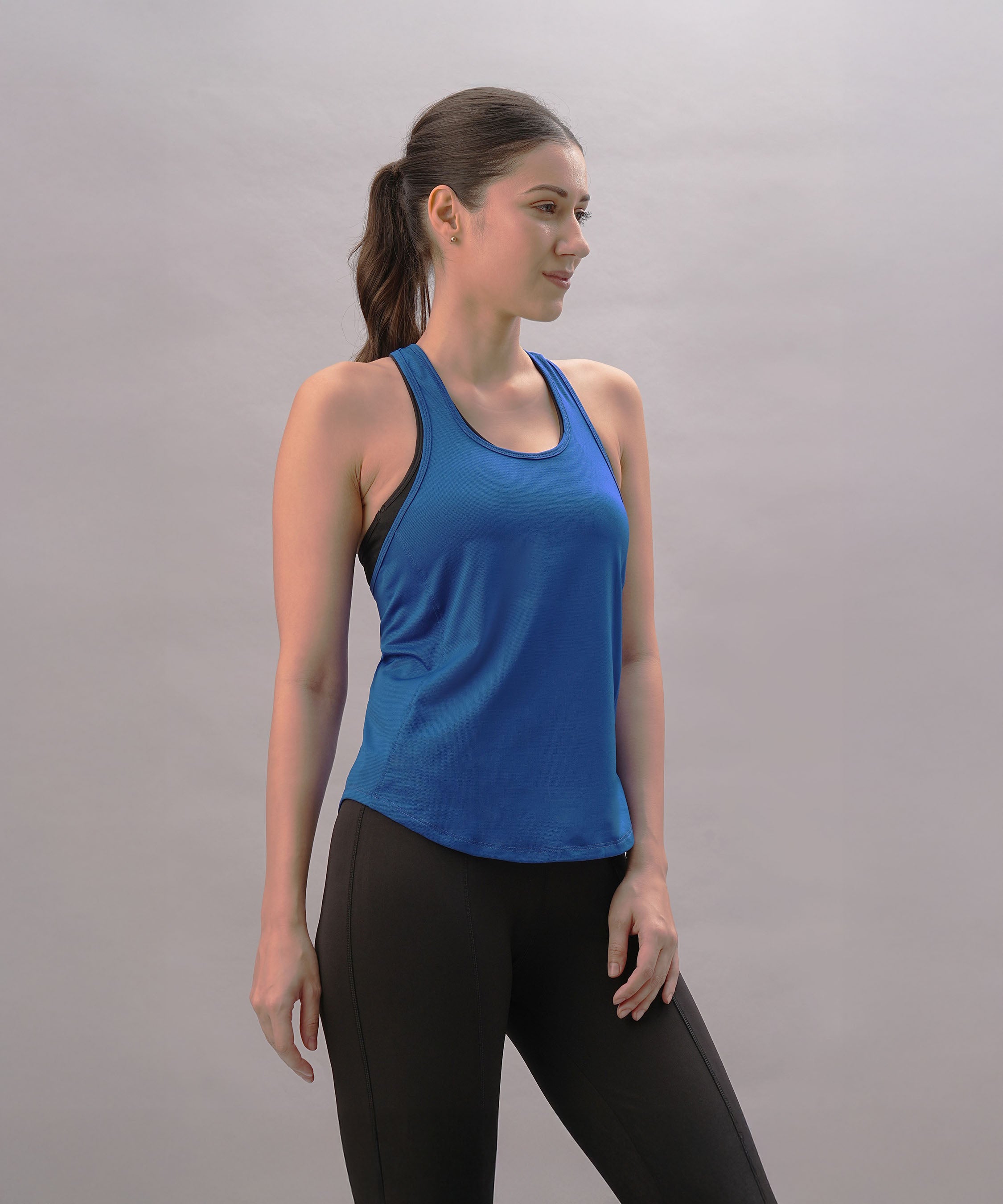 A woman models the Blue Racer Back Top with black leggings, standing against a plain light background to showcase this stylish activewear.