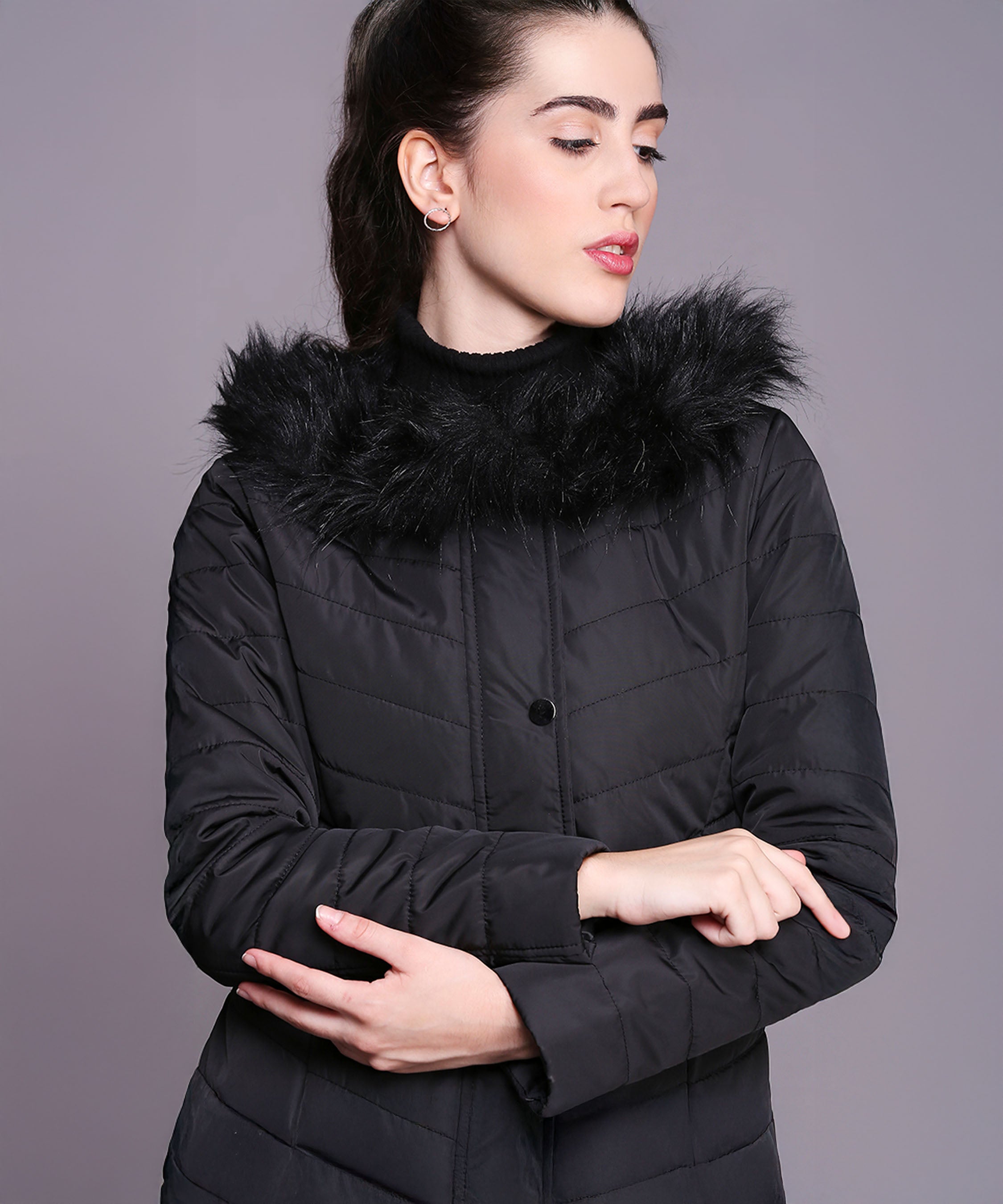 A woman poses with arms crossed against a grey background, wearing the Black Fur Collar Long Puffer Jacket With Button and Zip Details.