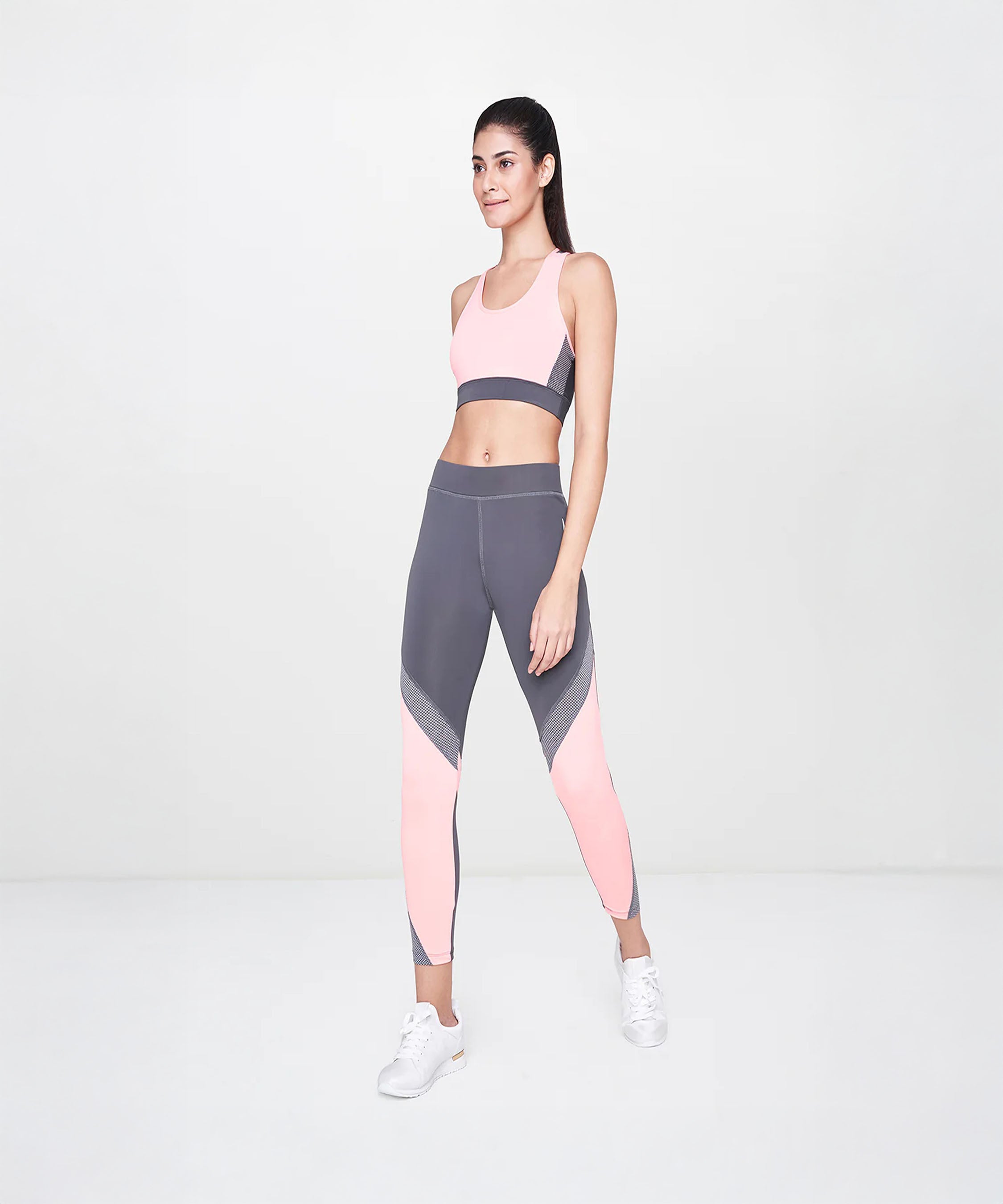 Woman in pink and gray sportswear poses confidently in a studio, highlighting her high-waisted Grey Leggings against a plain light background.