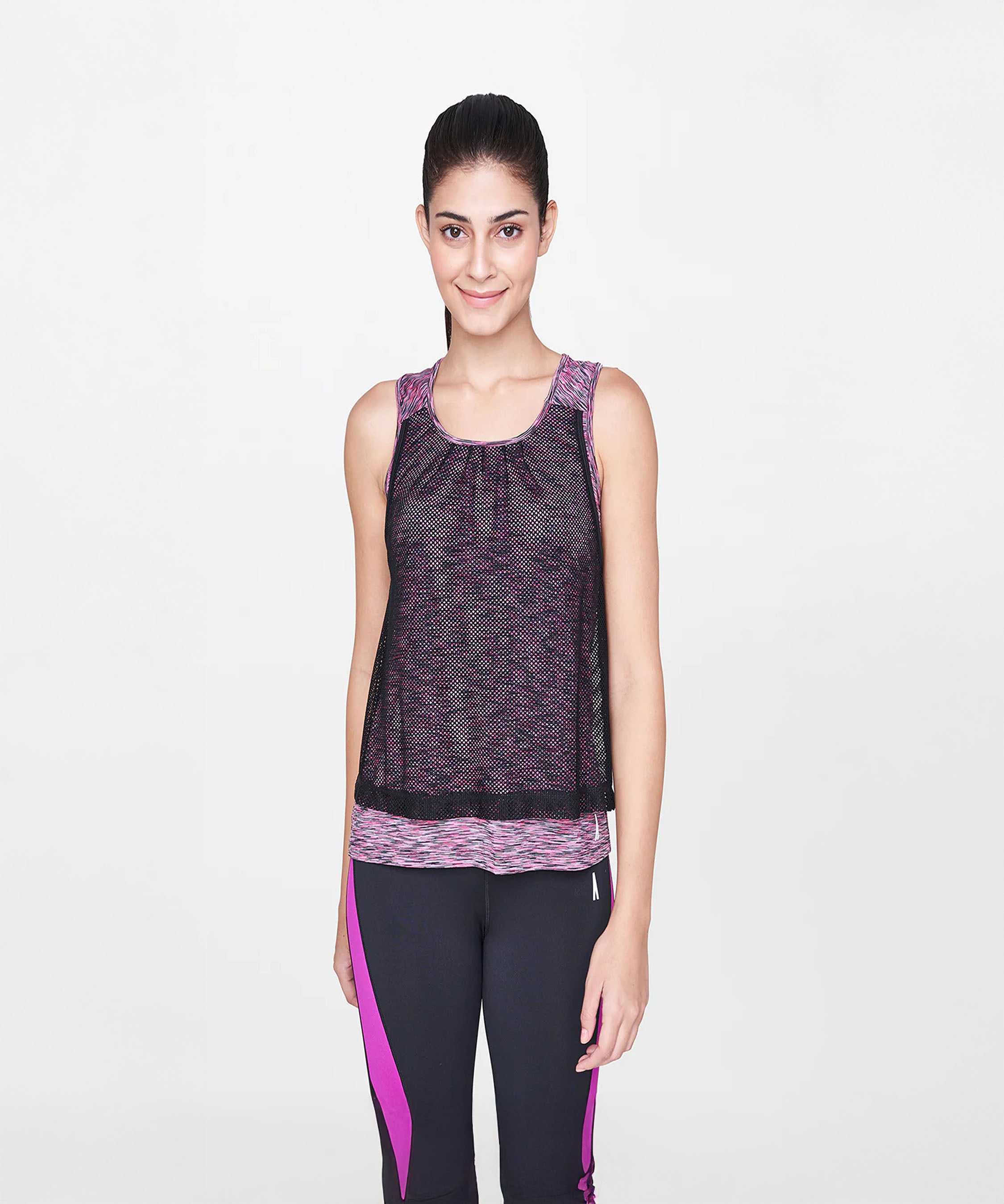 A woman stands smiling on a white background, wearing the Blush Pink Tank Top with a mesh overlay and black leggings with pink accents—perfect for any workout wardrobe.