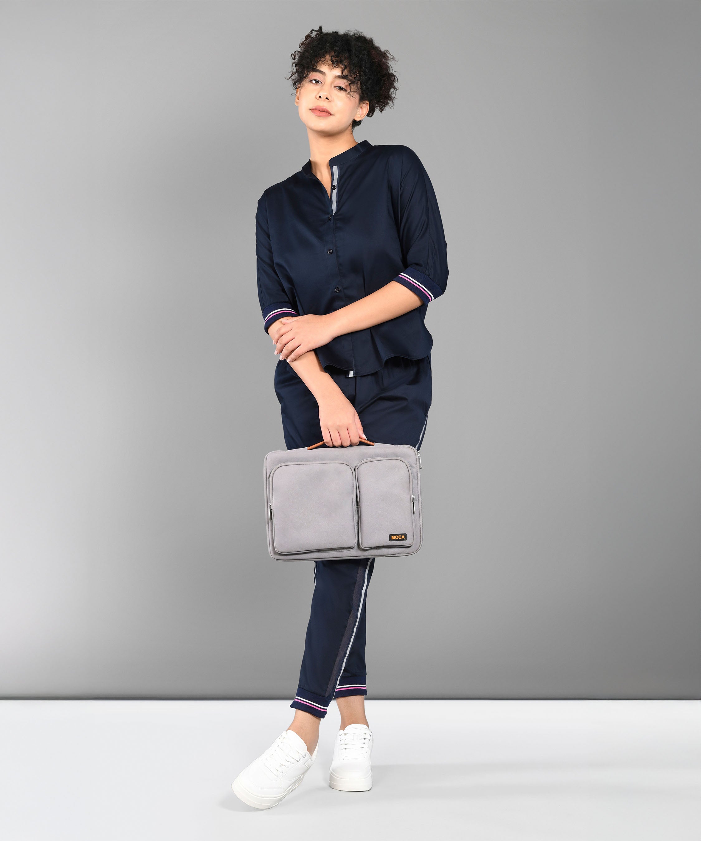 A person wears the Accented Set in navy blue cotton, paired with white shoes and holding a gray bag, standing before a plain gray background.