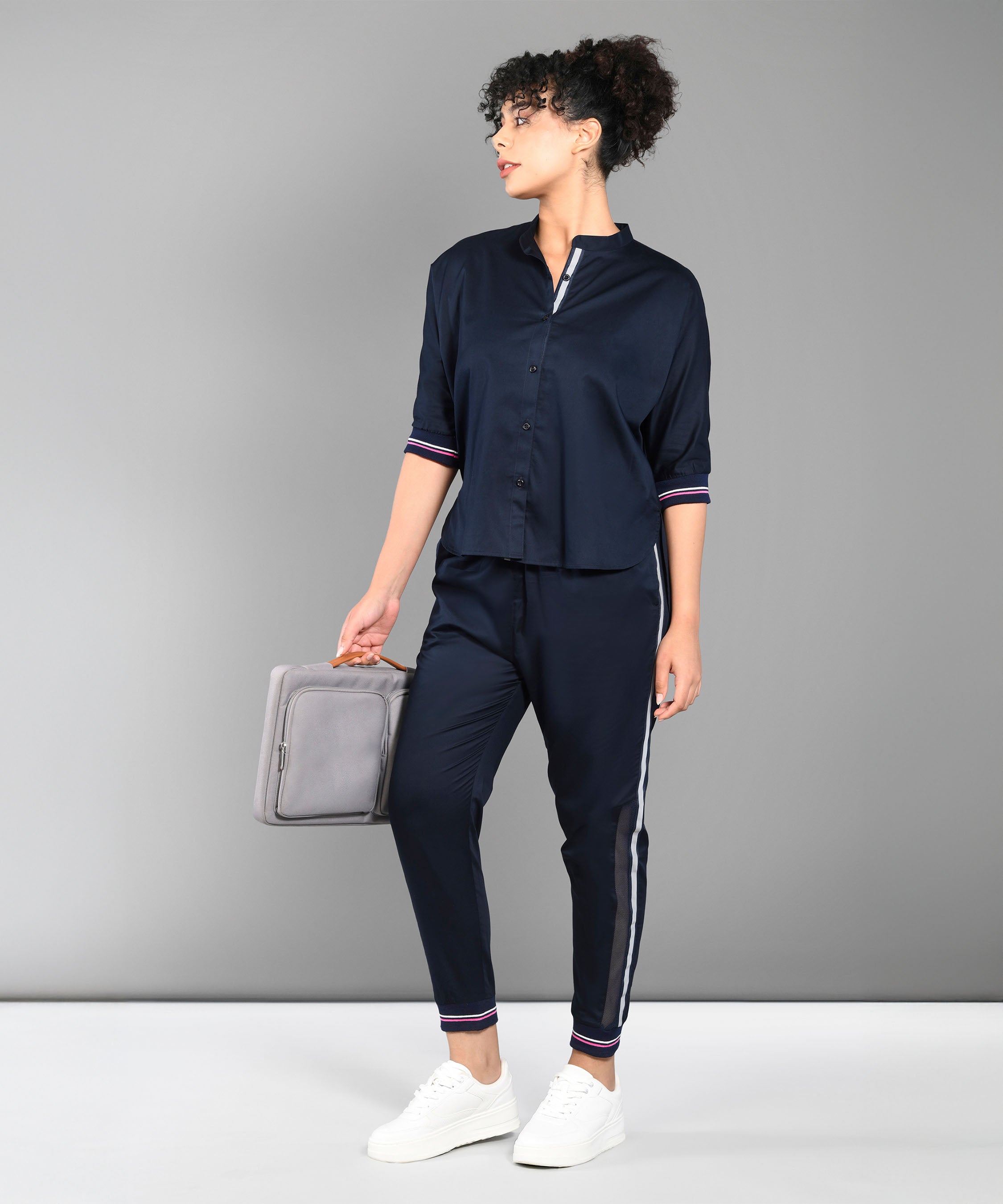 Woman wearing the Accented Set, paired with white sneakers and a gray bag, standing against a gray background.