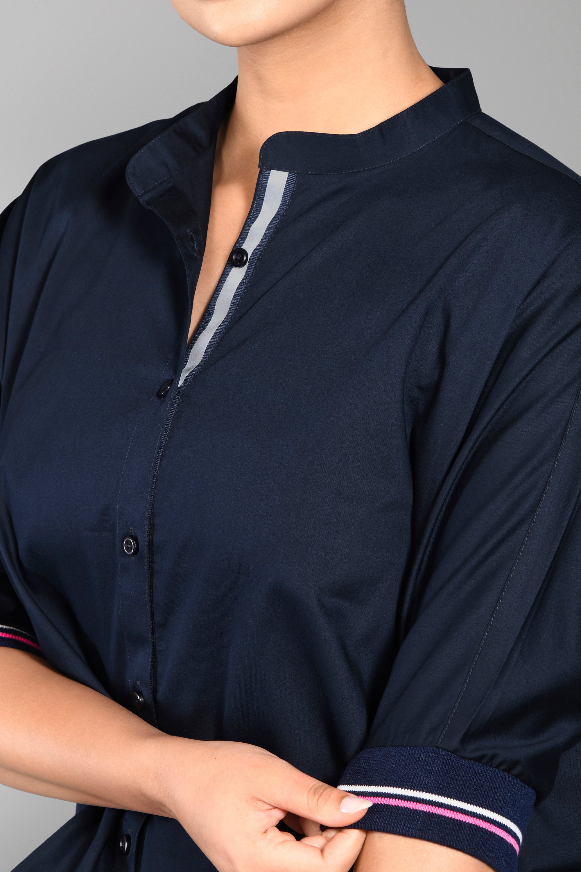 Model wears the Accented Set, a navy cotton co-ord featuring distinctive pink-striped sleeves, while adjusting the cuff on their shirt and matching joggers.