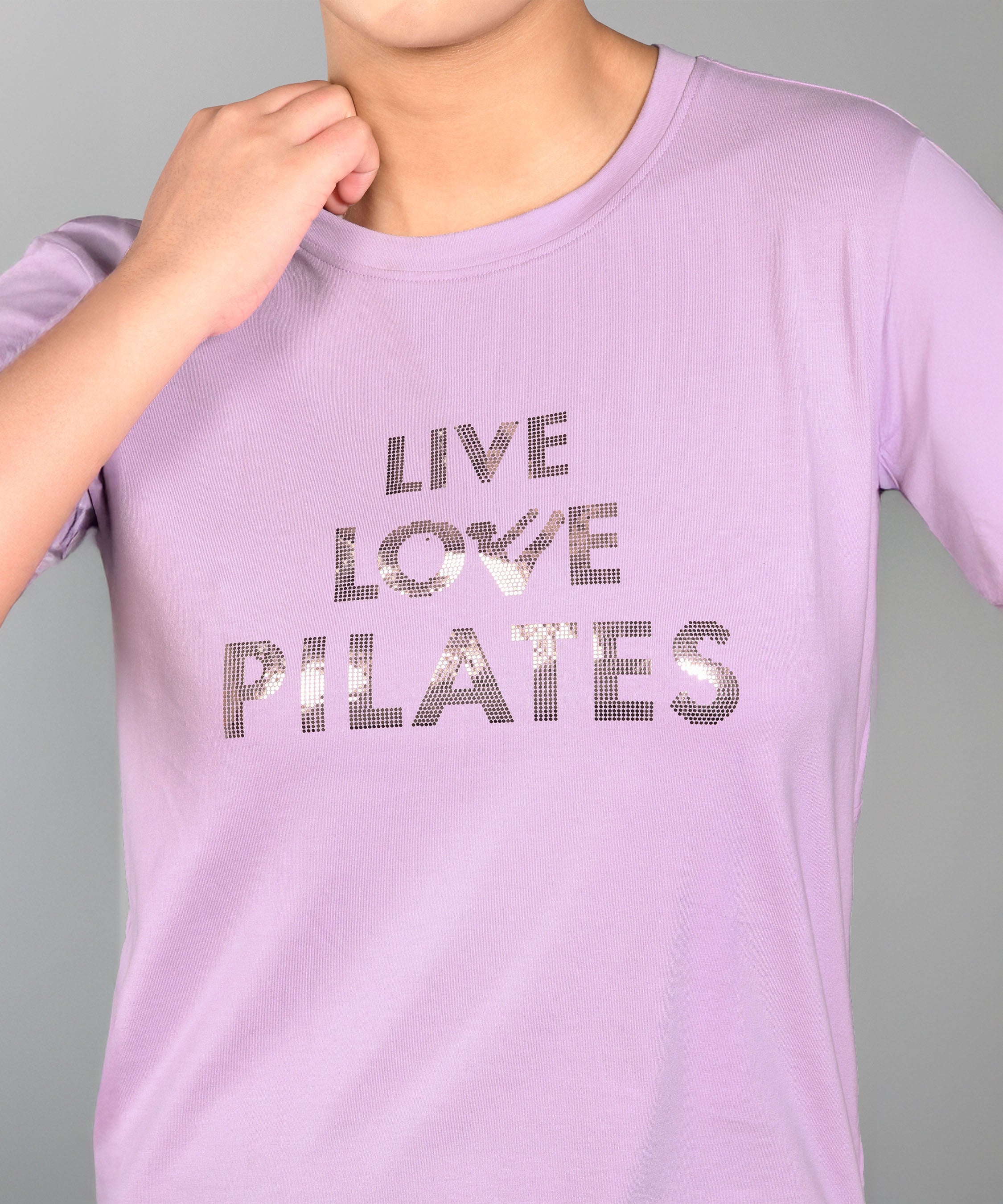 Woman in a Pilates Pink T-shirt with shiny lettering, hand near chin. This stylish and comfortable top enhances your active look.