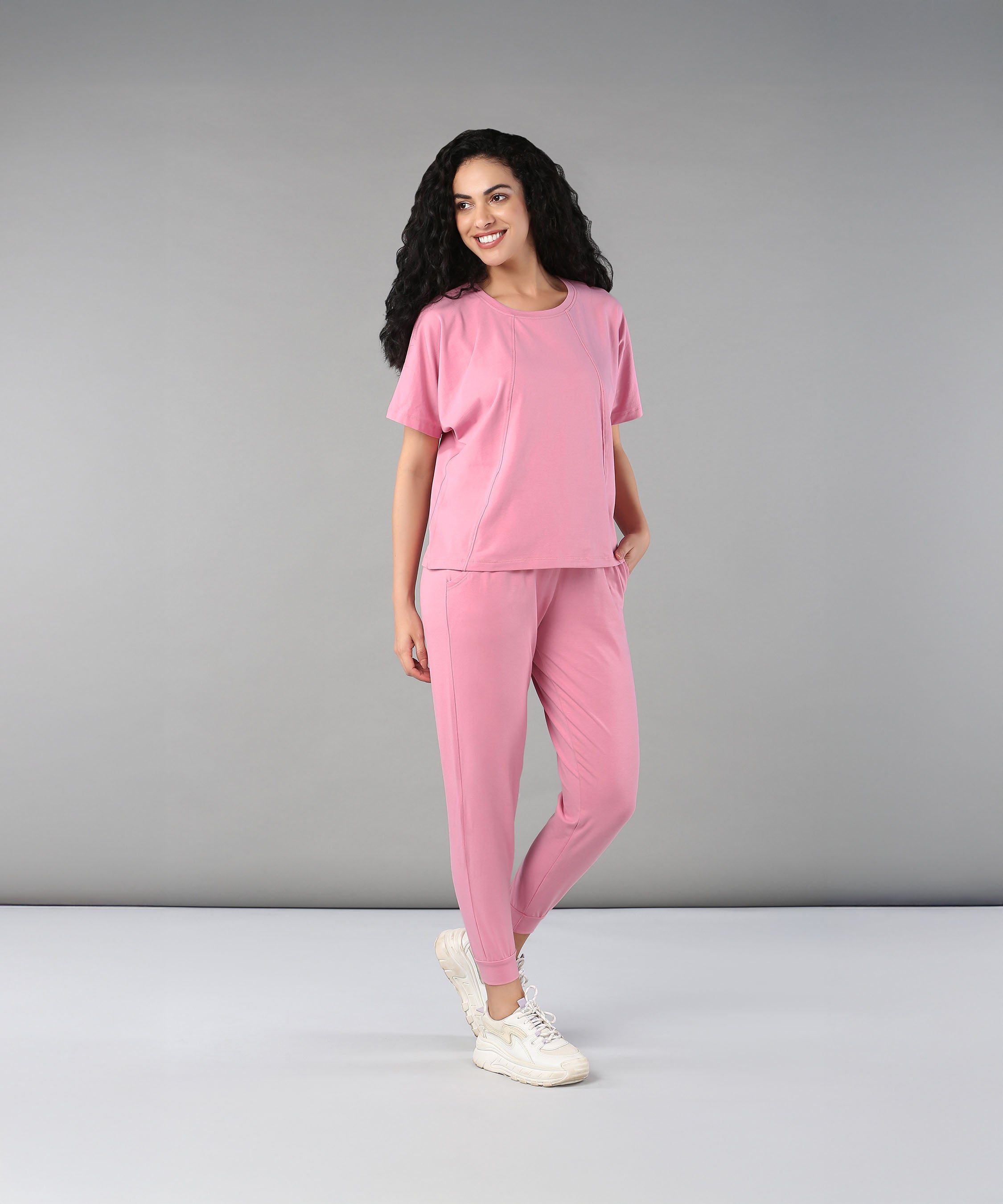 A woman with curly hair smiles against a plain background, wearing the Flamingo Pink Chic Ensemble. The buttery soft fabric brings comfort and style to her look.
