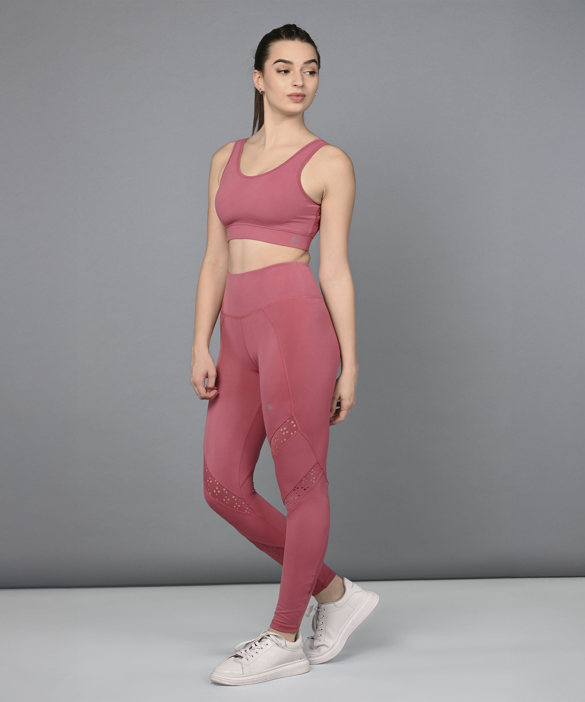 A woman wearing the Peony Pink Netted Top and matching leggings with white sneakers stands against a plain gray background.