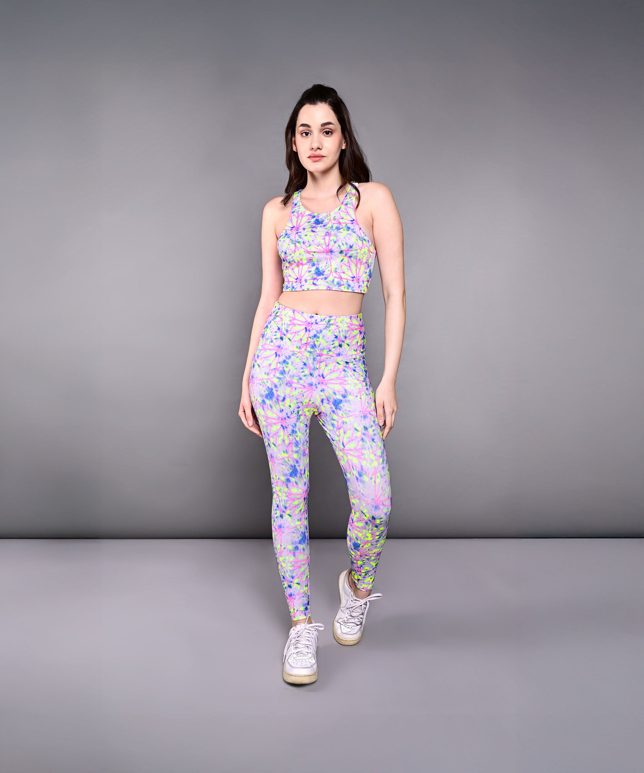 Woman in a comfortable, skin-friendly Multicolor Neon Crop Top and white sneakers poses against a plain gray background.
