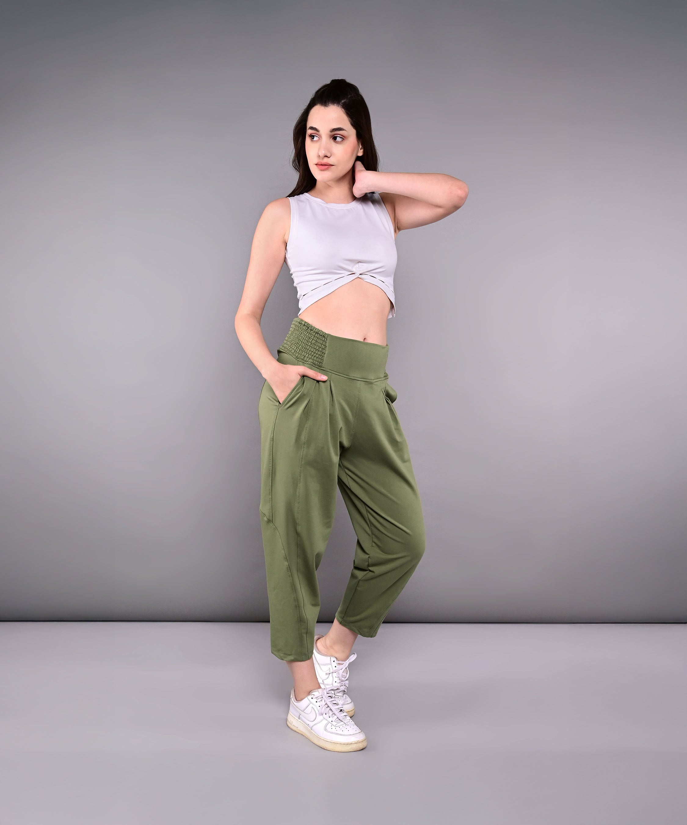 Woman wears green Pleated Yoga Pant With Smocked Waistband, featuring pleats and a high waist, paired with a gray sleeveless crop top and white sneakers.