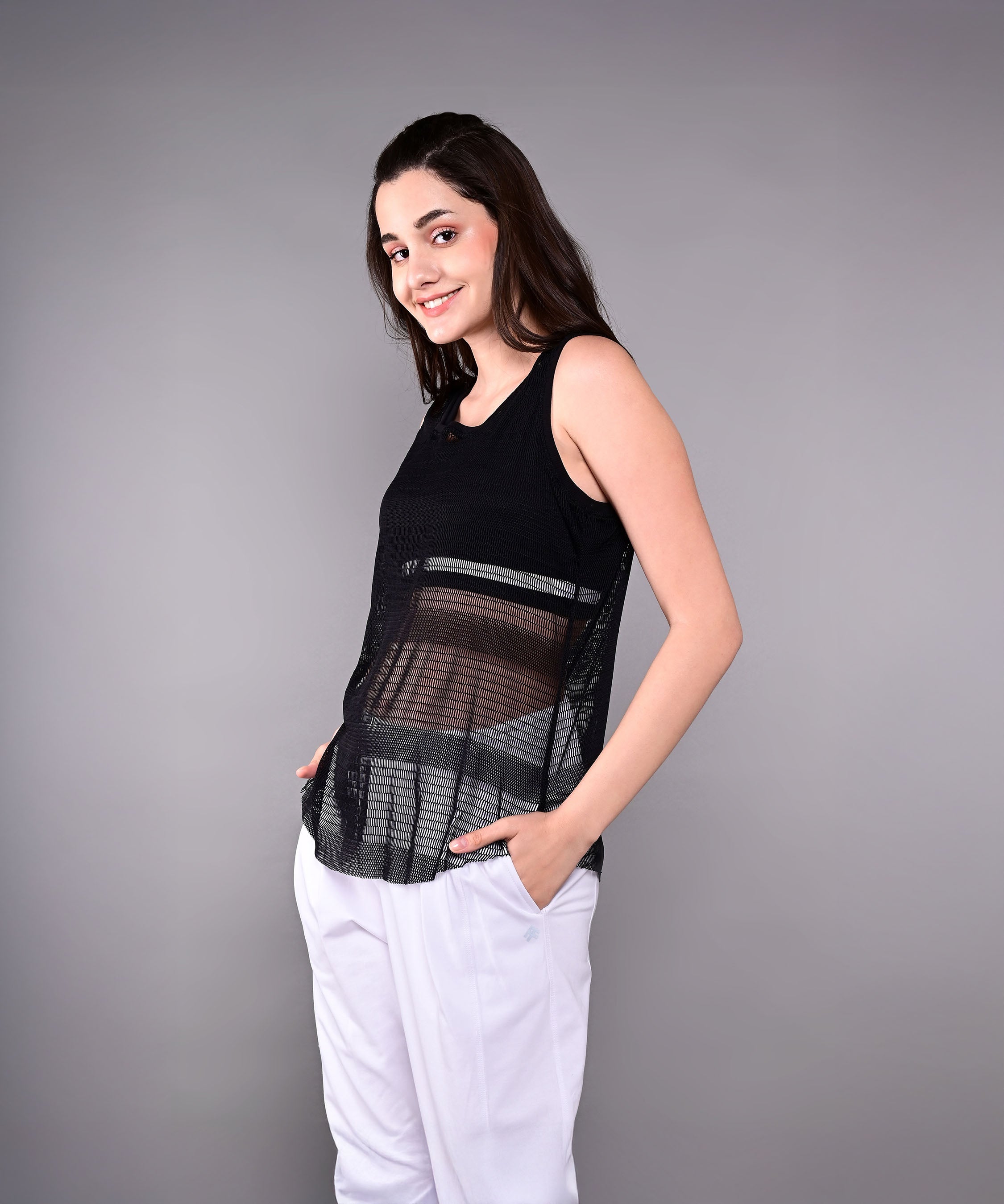 Model wears the Tuna Active Black Netted Tank Top with white pants, posing with hands in pockets against a gray background.