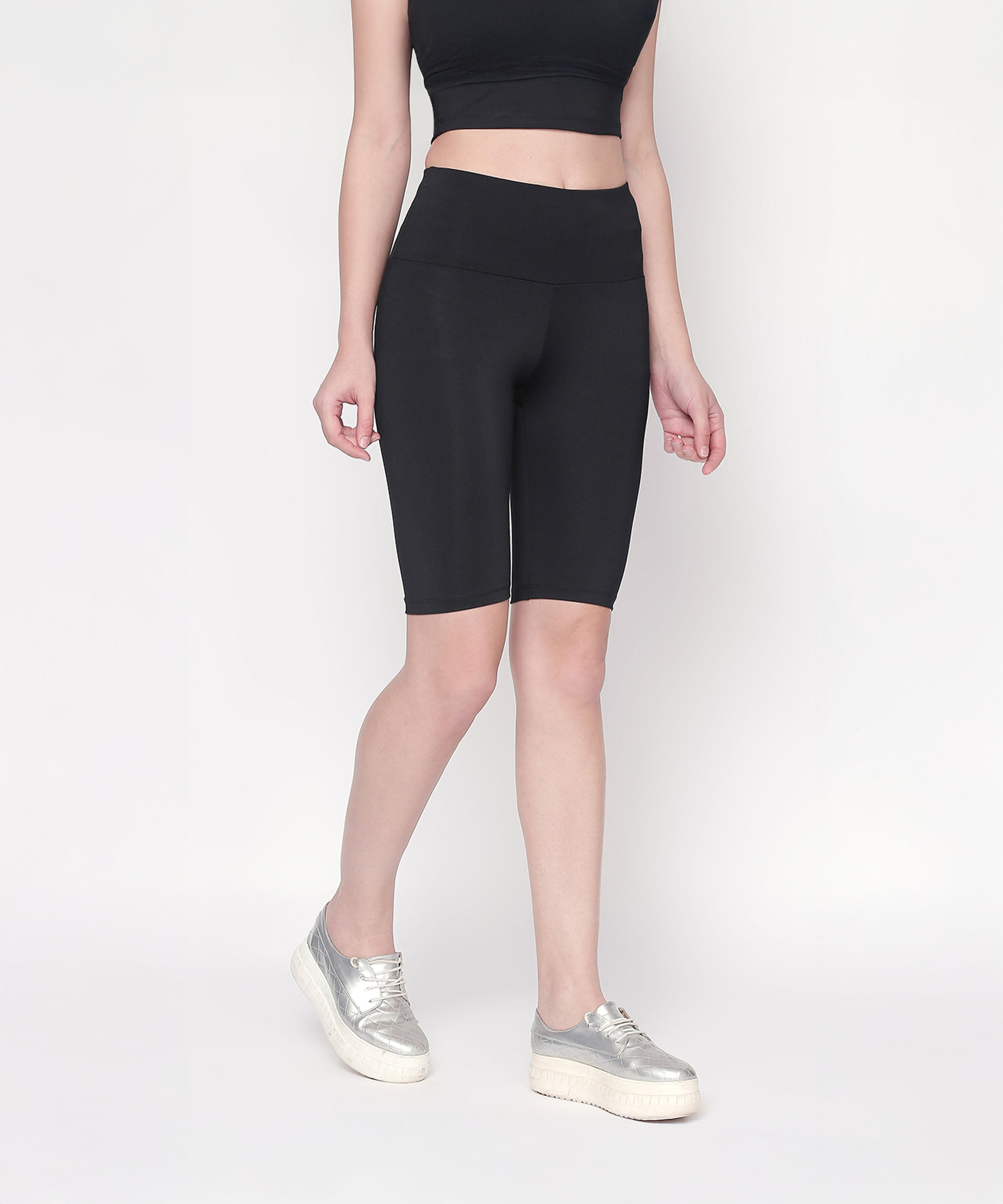 A person wearing Black Biker/Cycling Shorts with a high-rise waistband, a black crop top, and silver platform sneakers stands against a white background.