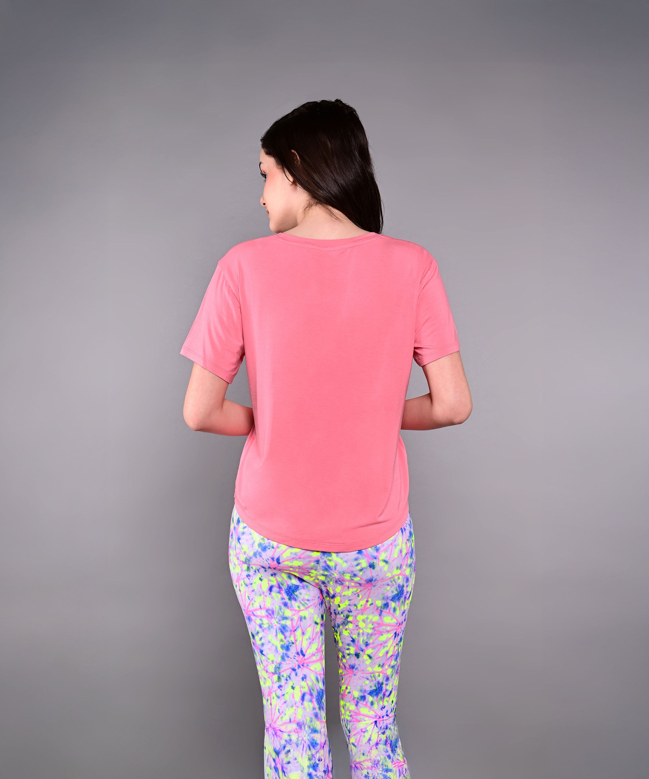 Woman with long dark hair stands with her back to the camera, wearing the pink 'Adore Your Core' Printed Tee and colorful patterned pants.