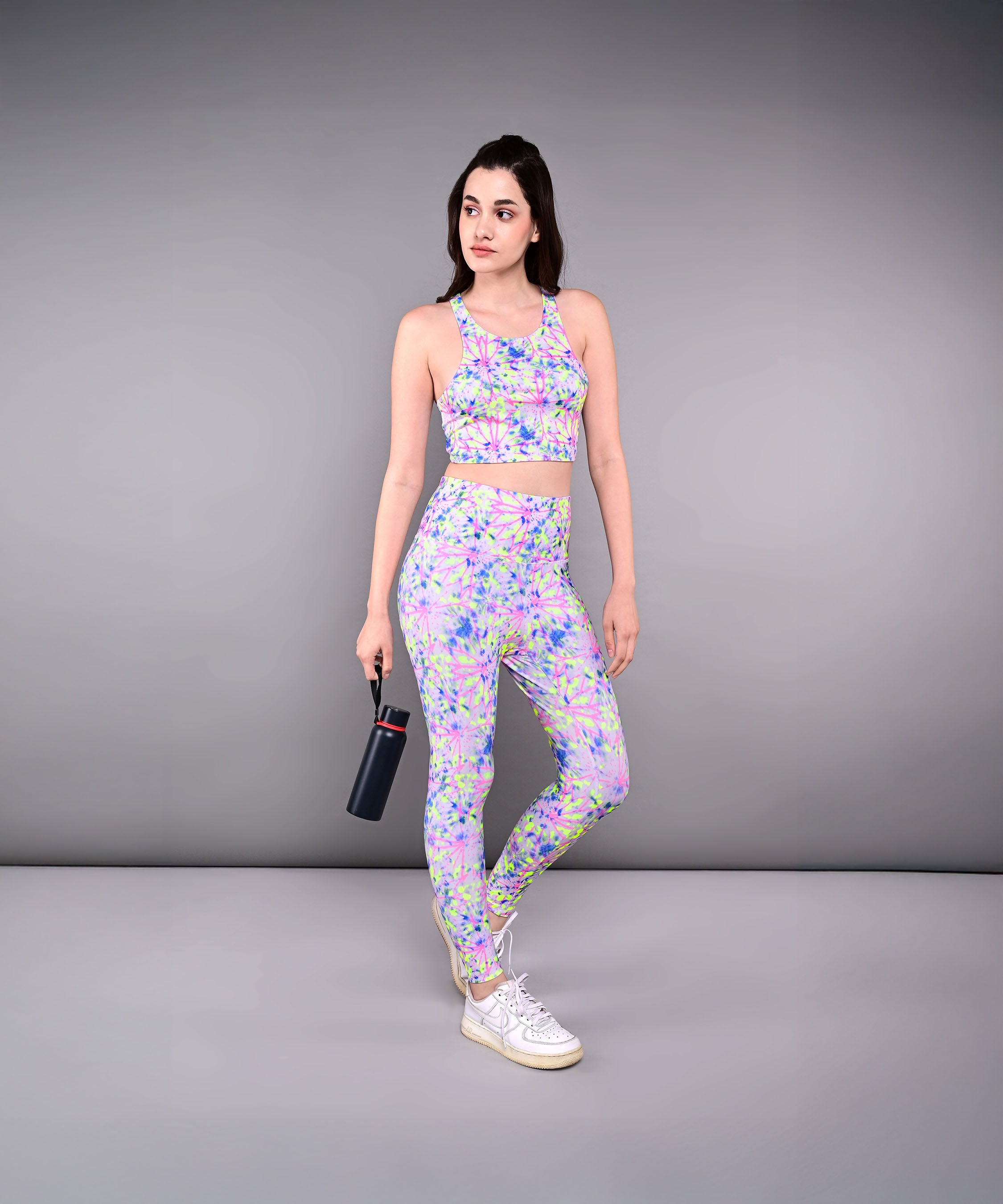 Woman wearing the Multicolor Neon Crop Top, made from skin-friendly cotton lycra, holds a water bottle while standing against a plain gray background.