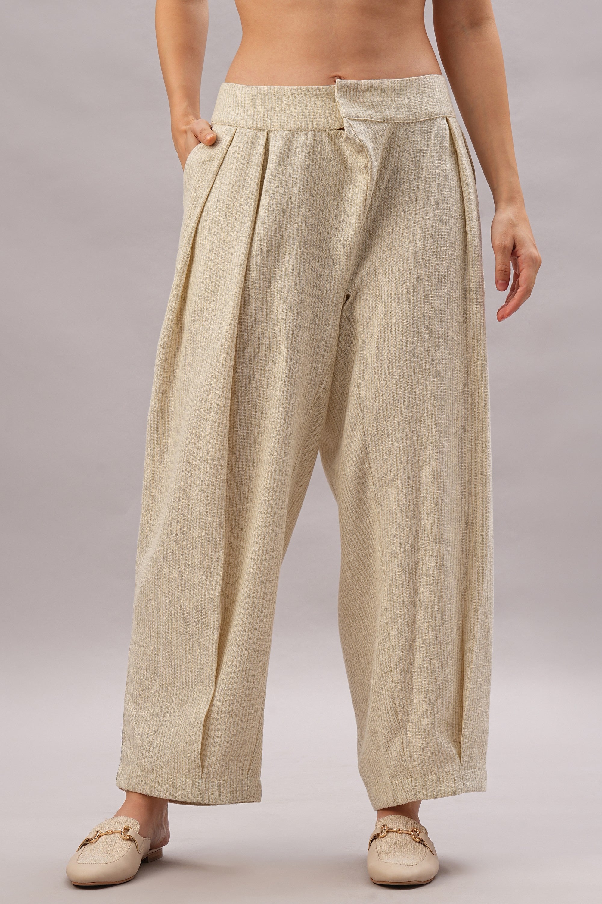Wearing the Beige Linen Set—loose, high-waisted pleated pants paired with cream loafers and a hand in the pocket—for effortlessly stylish comfort in breathable linen.