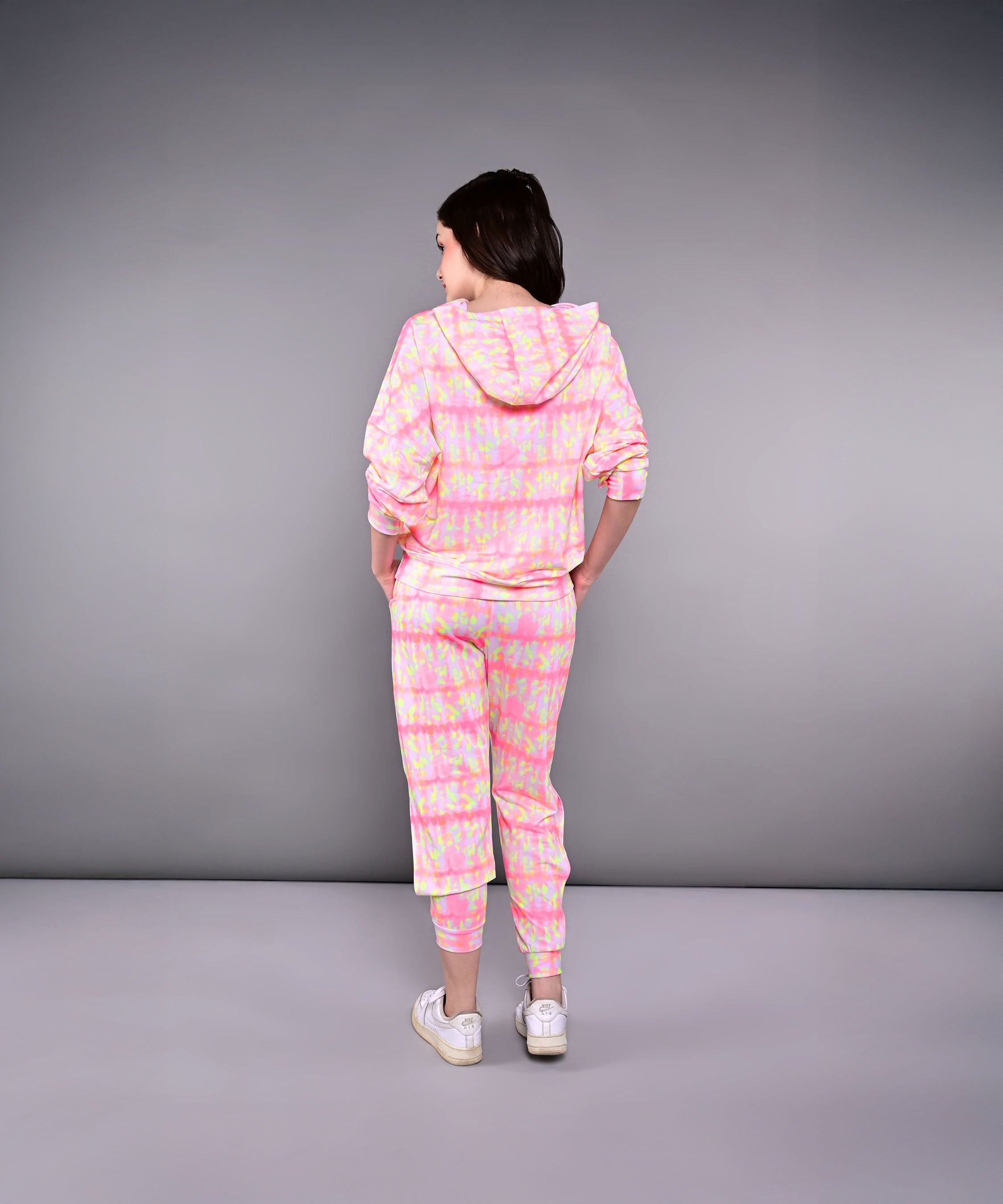 A woman stands with her back to the camera, wearing the Comfort Fit Tie-Dye Sweatshirt With Joggers Set in pink and yellow.