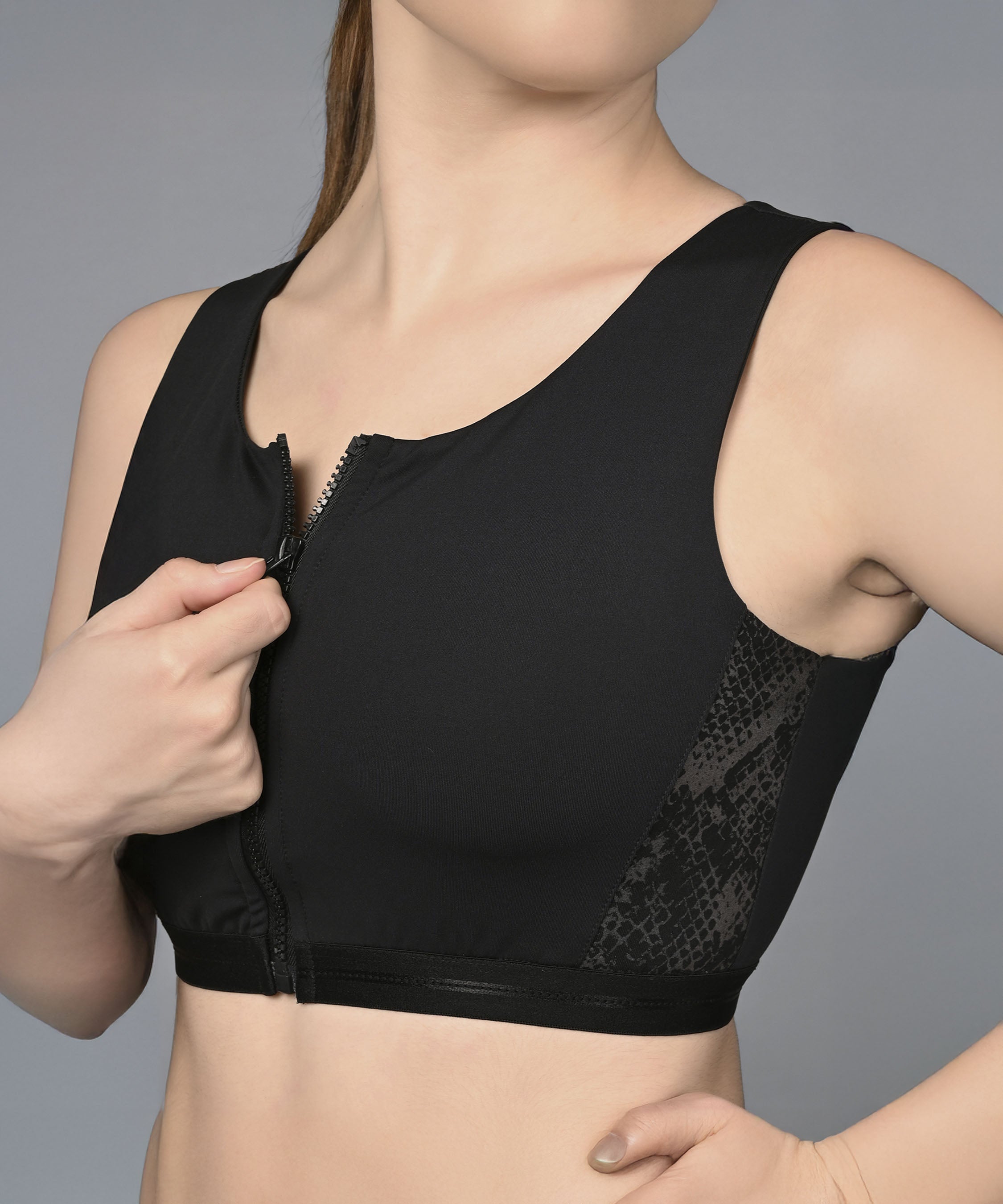 Model wears the Zipped Sports Bra, zipping it up against a plain gray background, paired with Metallic Legging for a chic and stylish activewear look.