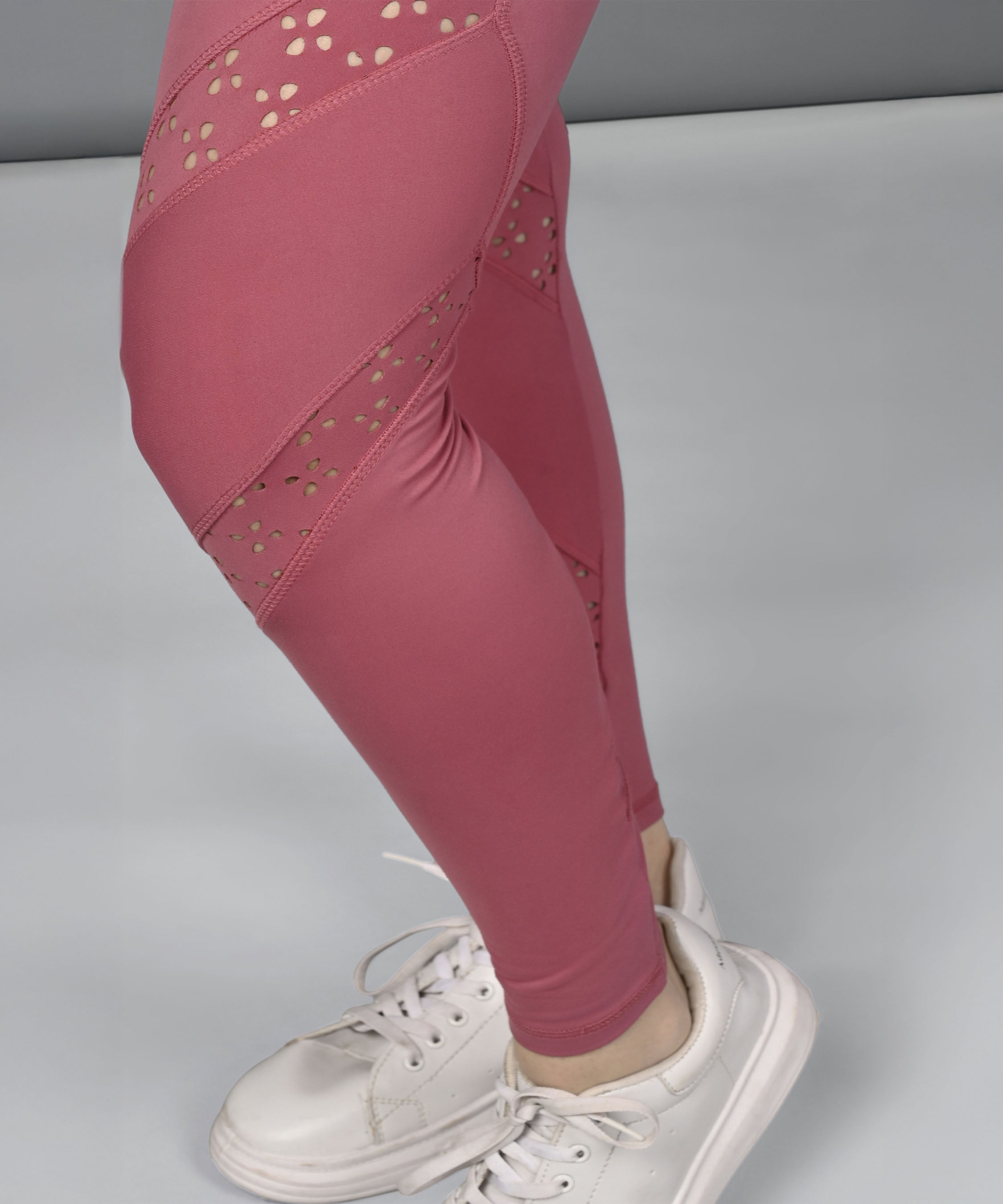 A person wears a Peony Pink Netted Top, pink cut-out leggings, and white sneakers while standing on a light gray surface.