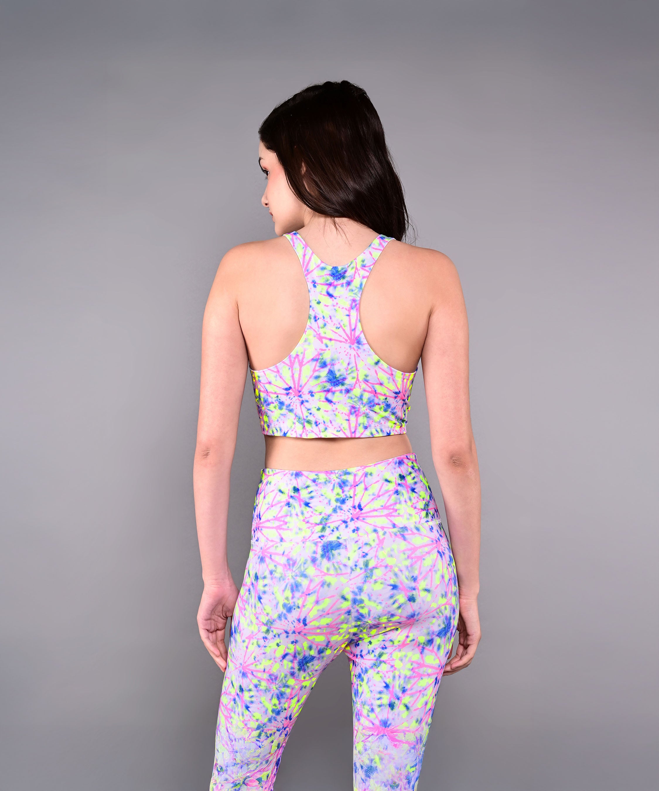 A woman faces away, wearing the Multicolor Neon Crop Top in a skin-friendly cotton lycra floral print with matching leggings, set against a gray background.