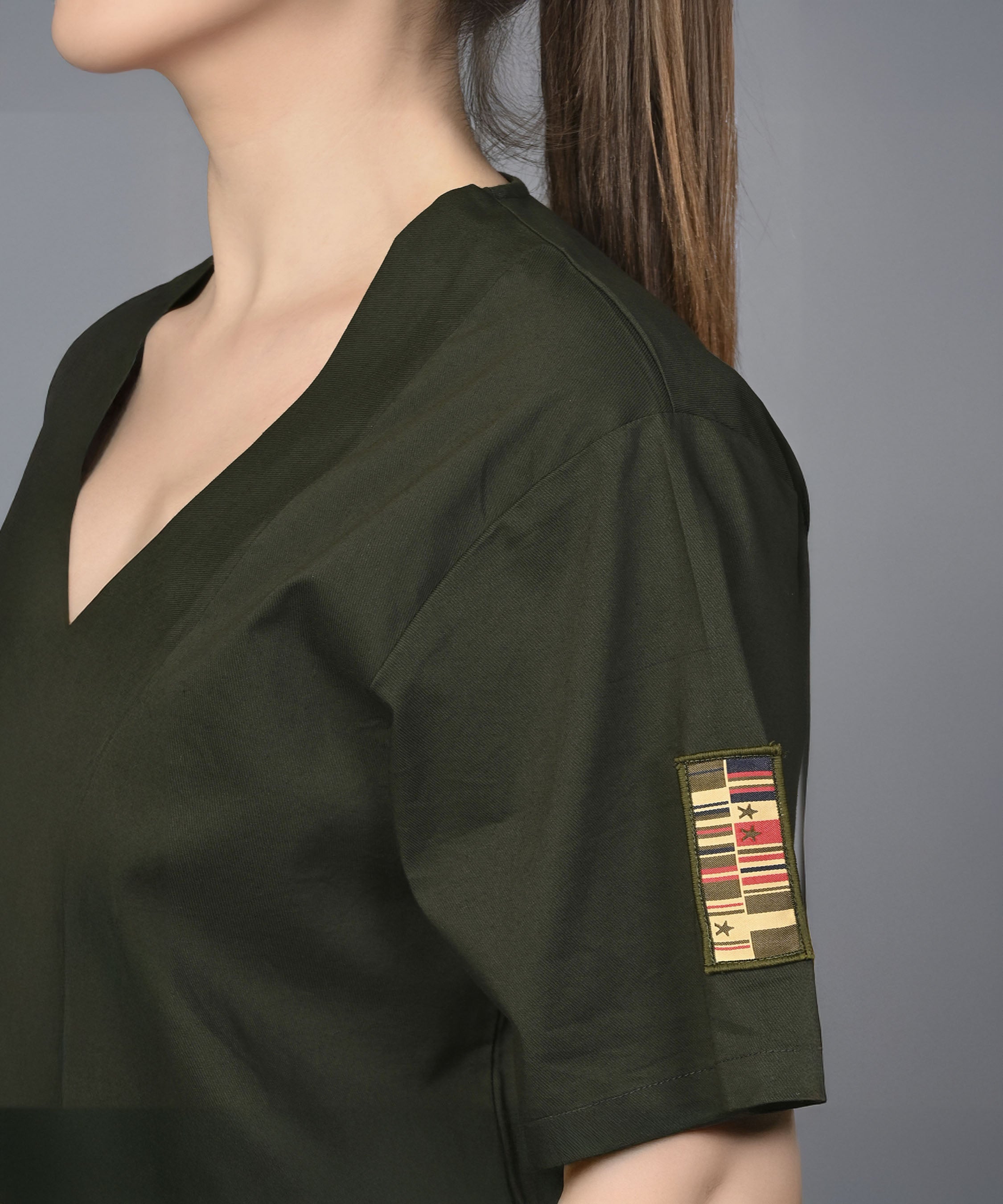 Wearing the Military Green Open Jacket & Yoga Pants with Bustiere set, a person in a dark green top featuring a military-style patch achieves a modern, active look.