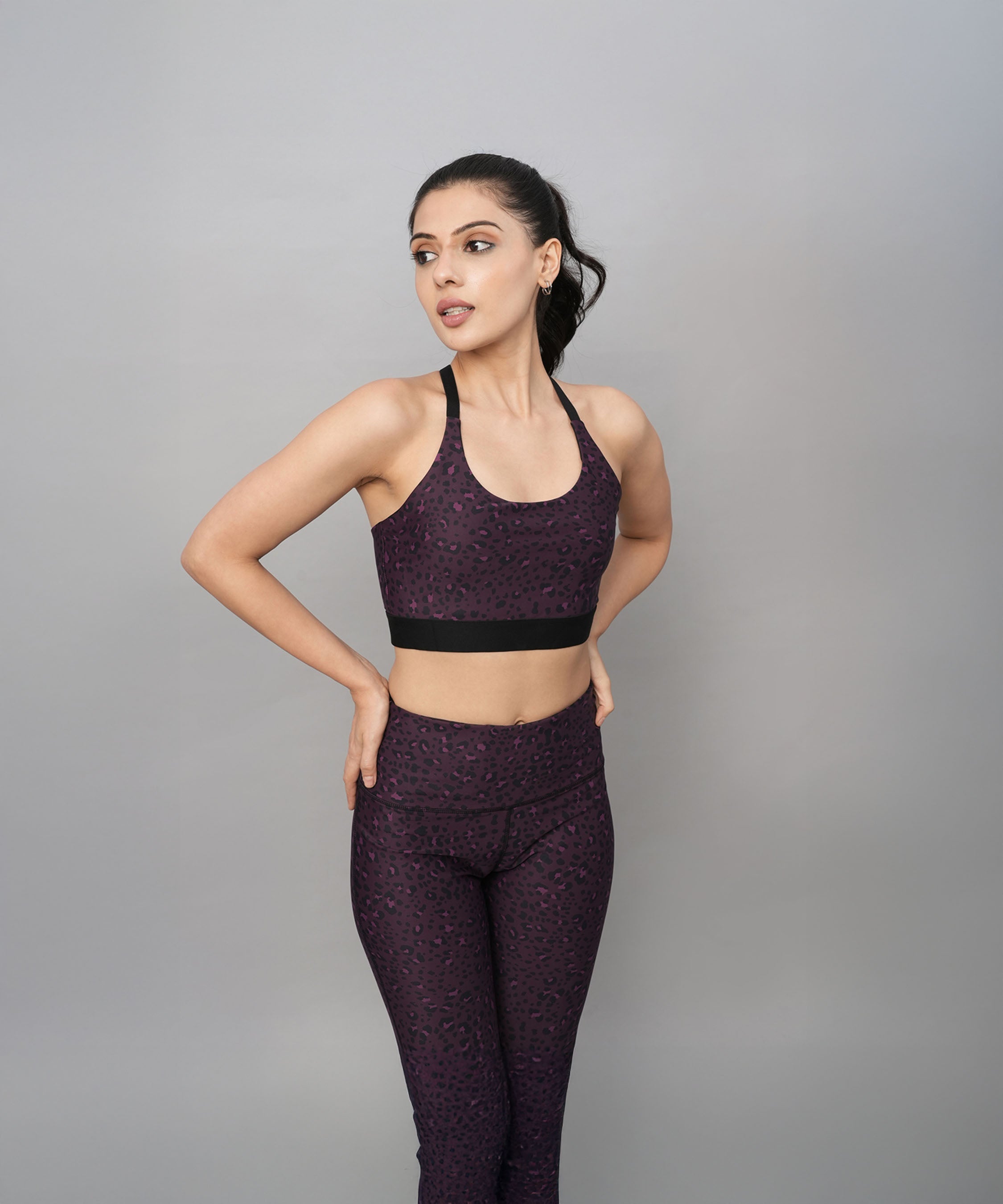 A woman poses confidently against a plain gray background wearing the Pink Animal Print Sports Bra.