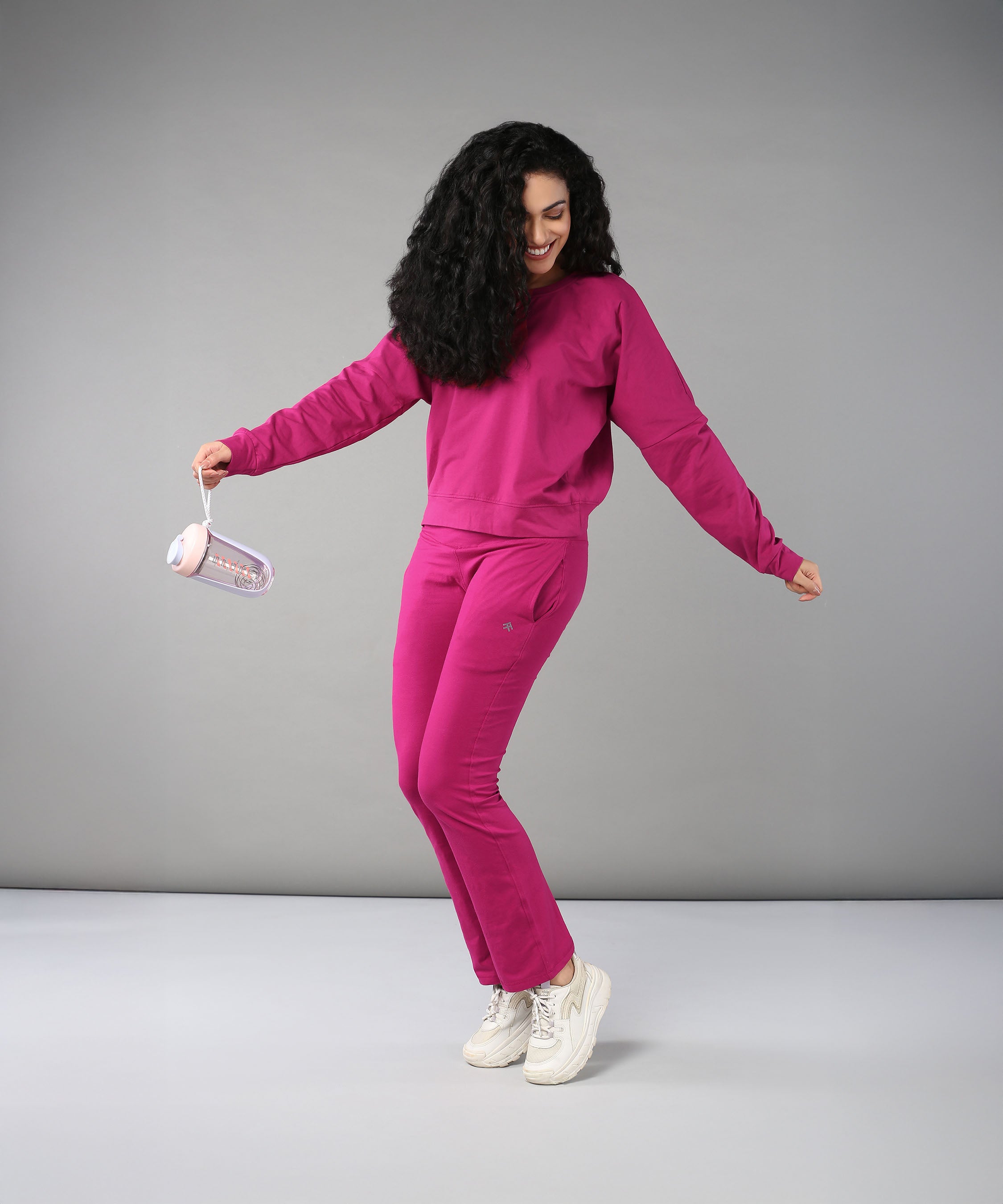 A woman in the Deep Pink Comfort Duo smiles while holding a water bottle and posing against a gray background, wearing comfortable cotton lycra activewear.