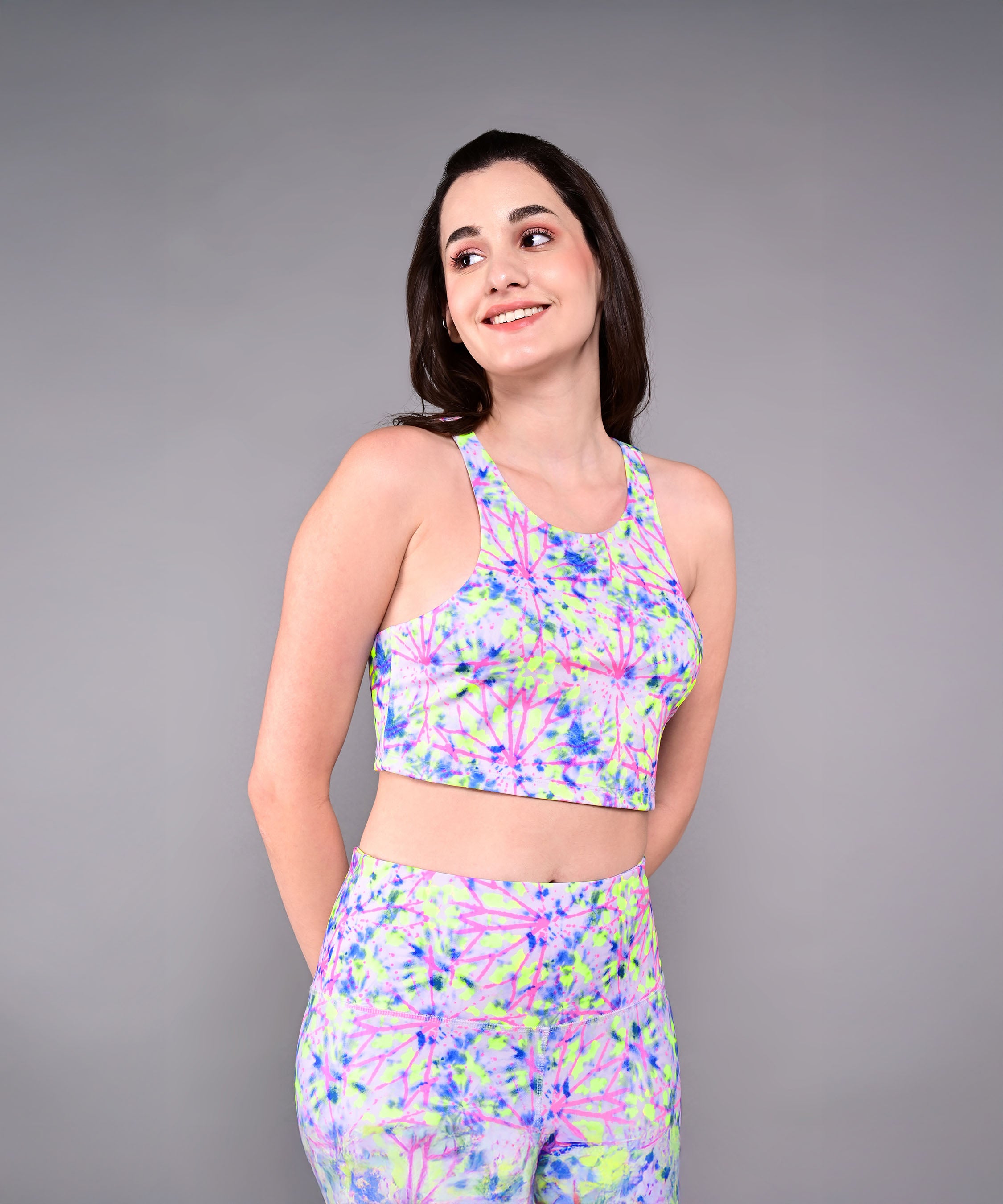 Woman smiles while looking to the side, wearing Multicolour Neon Leggings against a plain gray background.