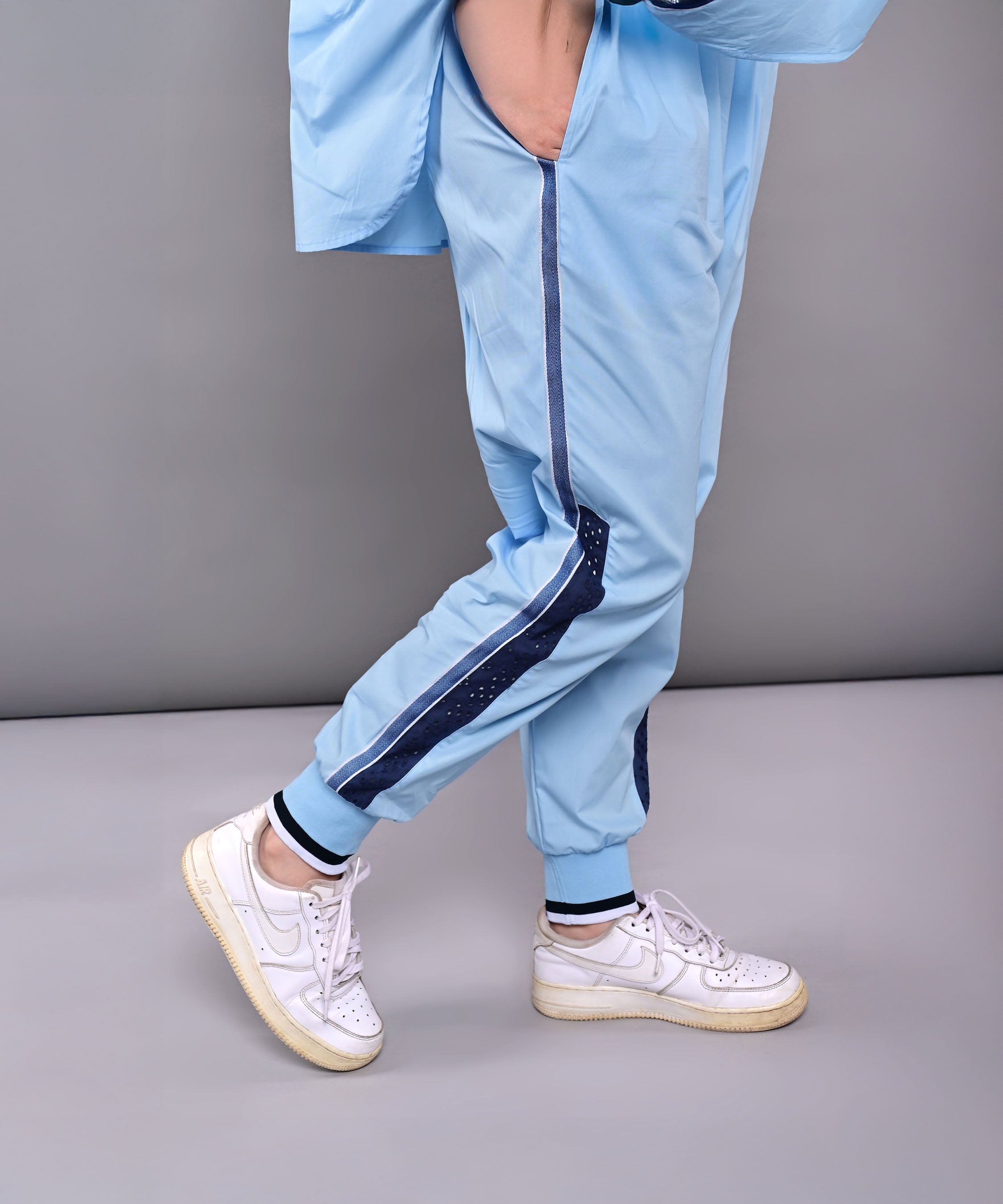 Wearing the Denim Accented Set, a person stands against a gray background in light blue pants and a 100% cotton batwing sleeve shirt, finished with white sneakers.