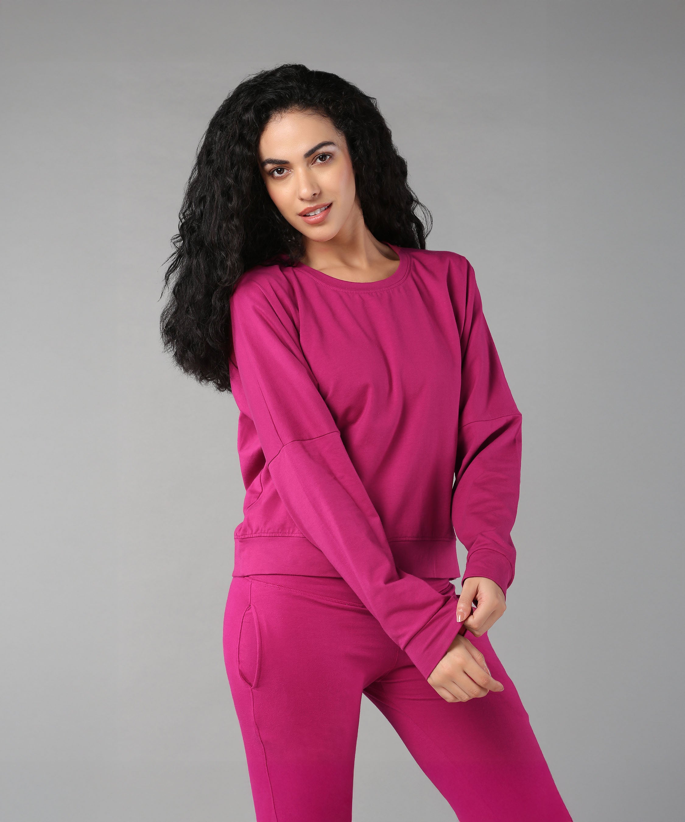 Woman with long curly hair wearing the Deep Pink Comfort Duo, standing against a plain gray background.