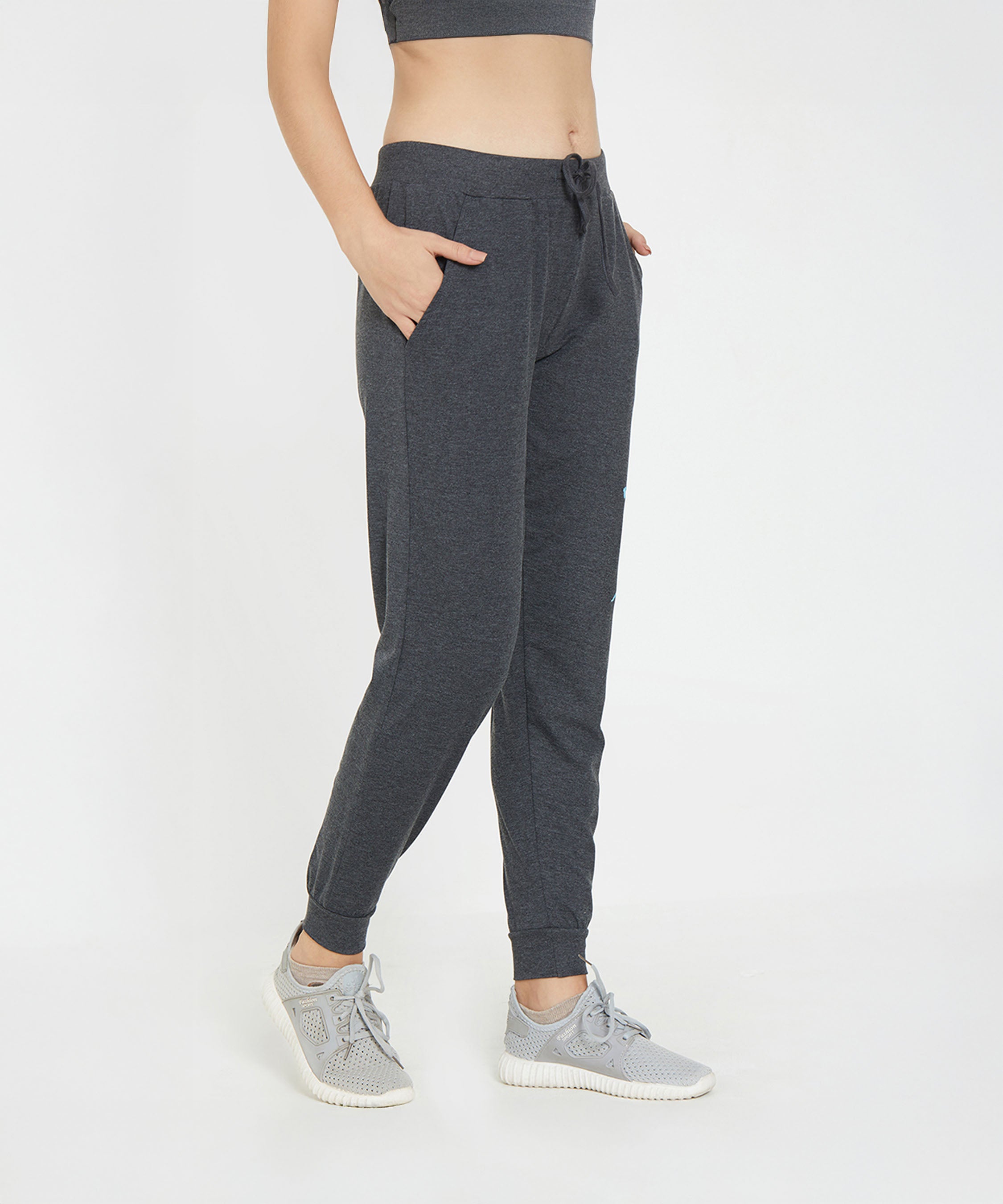 Woman wearing Joggers - Ashtanga Series Grey from TUNA LONDON with grey sneakers, standing hands in pockets against a white background.
