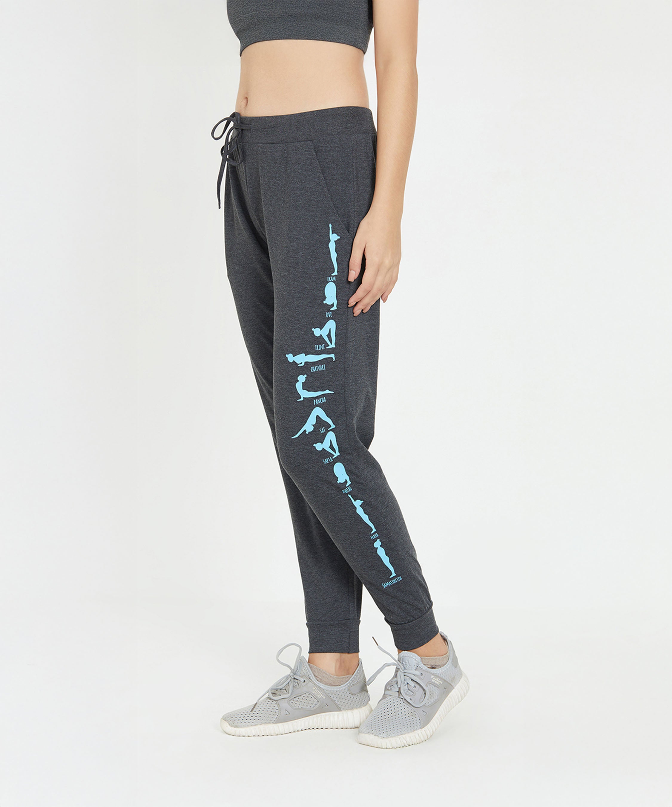 A woman in TUNA LONDON Joggers - Ashtanga Series Grey with blue text on the leg, a grey crop top, and grey sneakers, standing sideways.