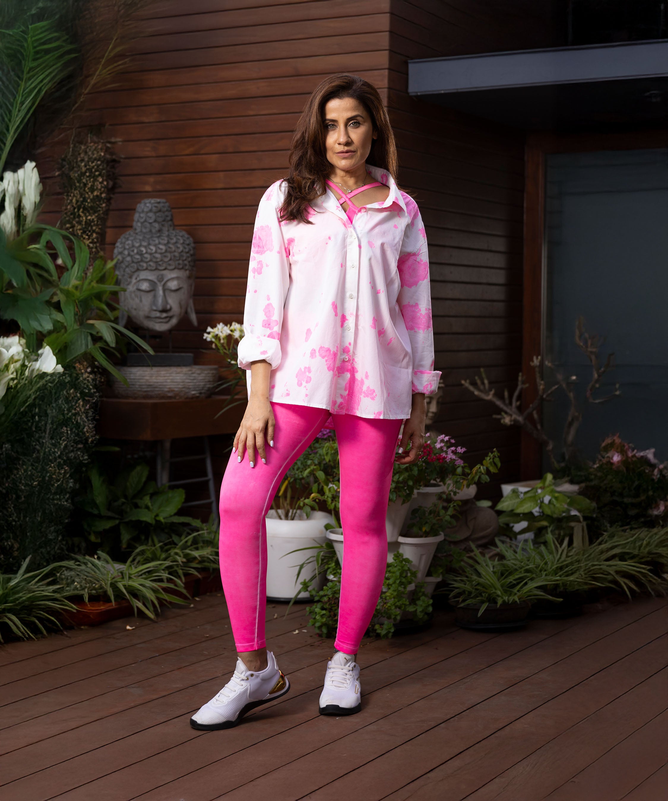 A woman in the Pink Patched Perfection shirt and bright pink leggings stands on a wooden deck surrounded by plants.