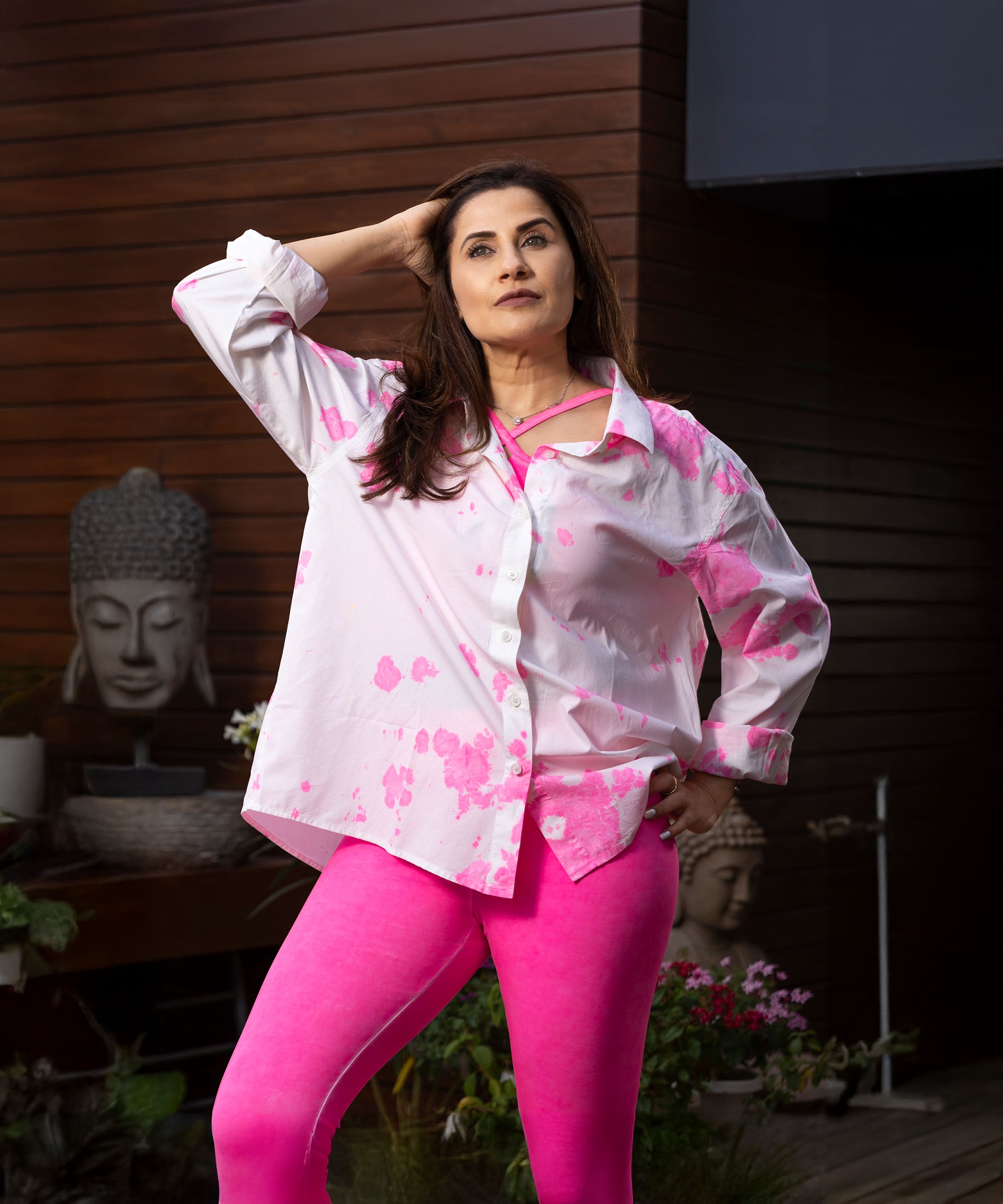 A woman stands confidently with one hand on her hip and head, wearing Pink Patched Perfection leggings and a pink and white printed shirt with adjustable straps.