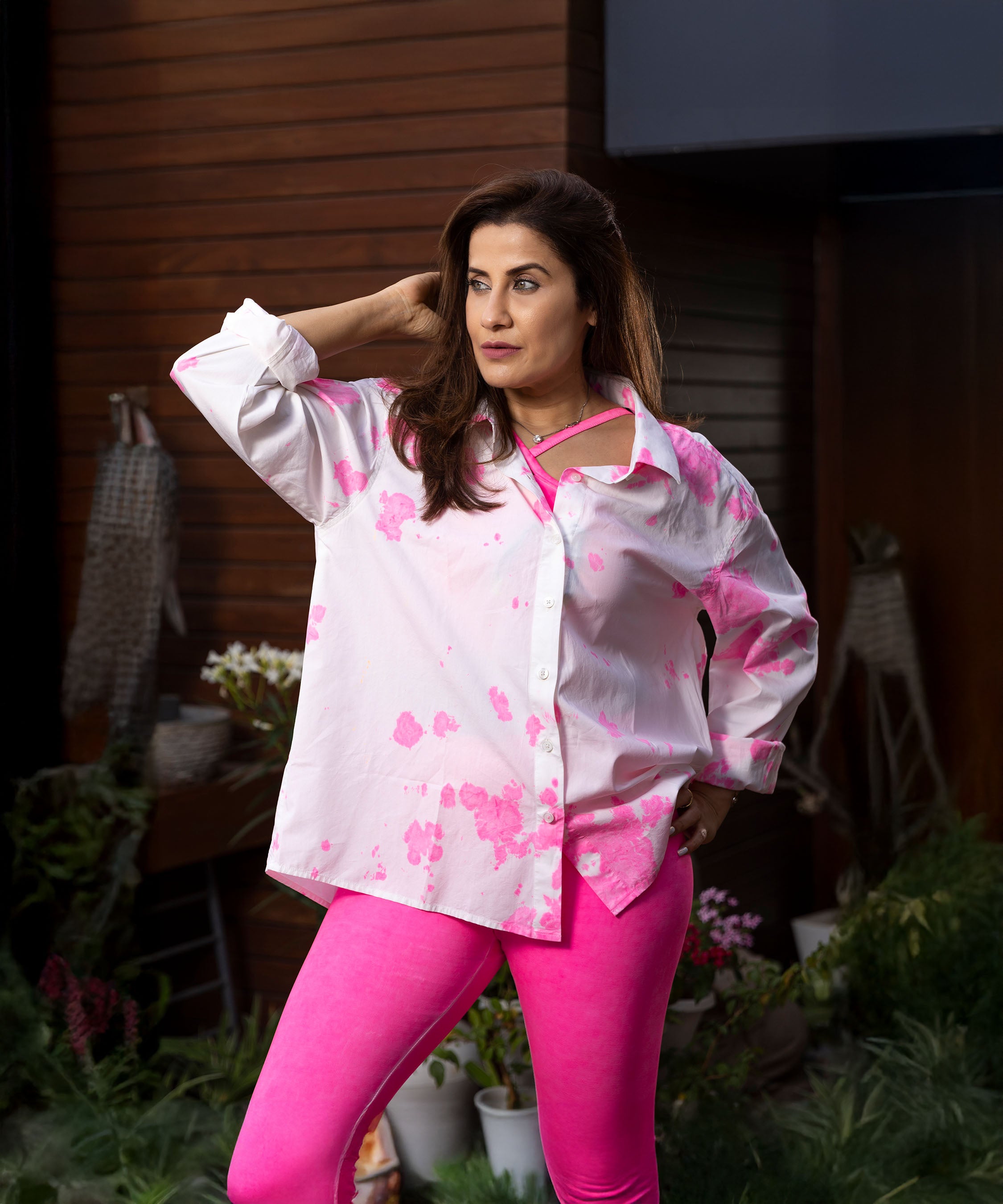 A woman stands outside among plants, wearing the "Pink Patched Perfection"—a pink and white printed shirt paired with pink leggings.