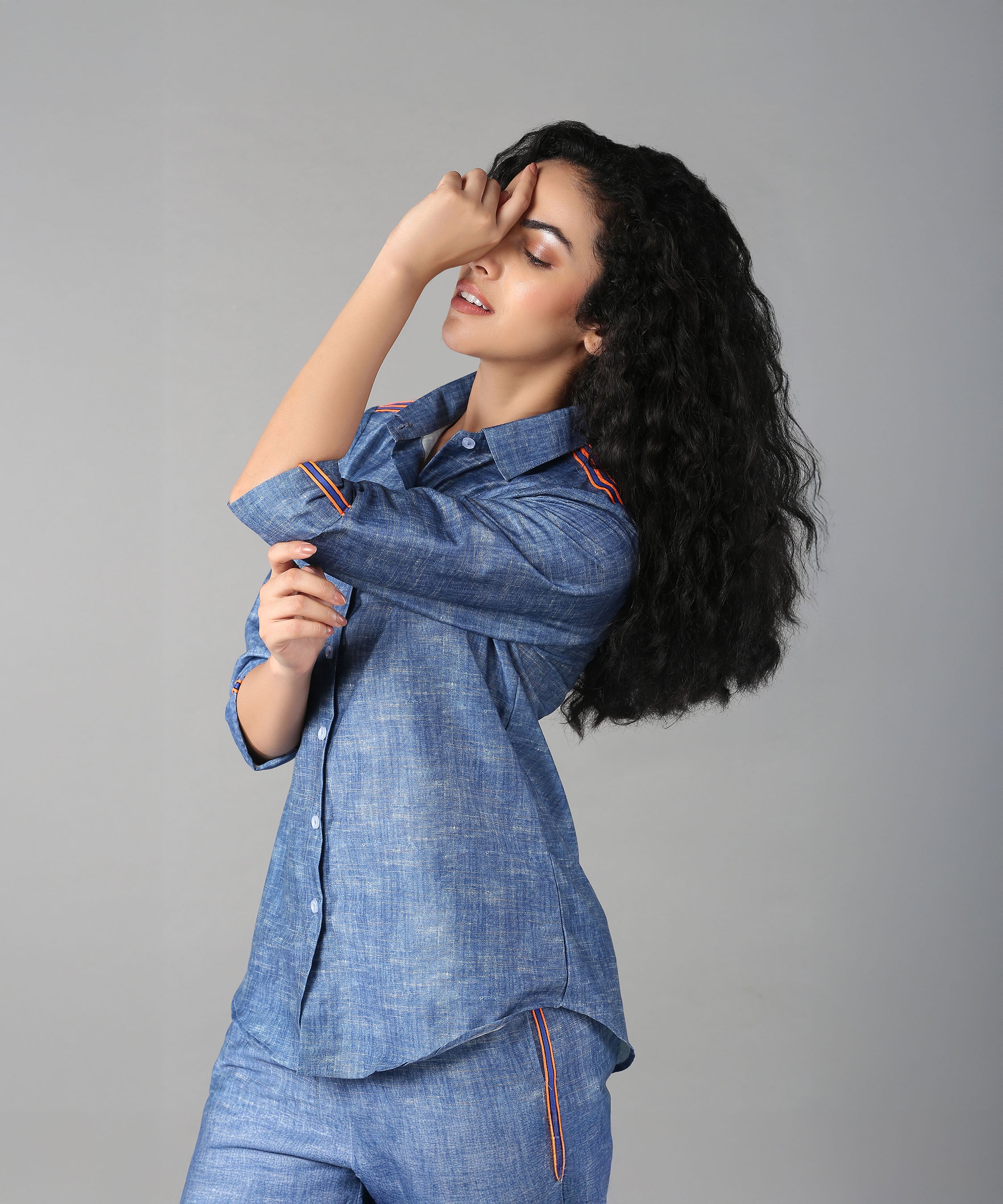 A woman with long curly hair poses in a relaxed fit Denim Linen Co-Ord Set, touching her forehead.