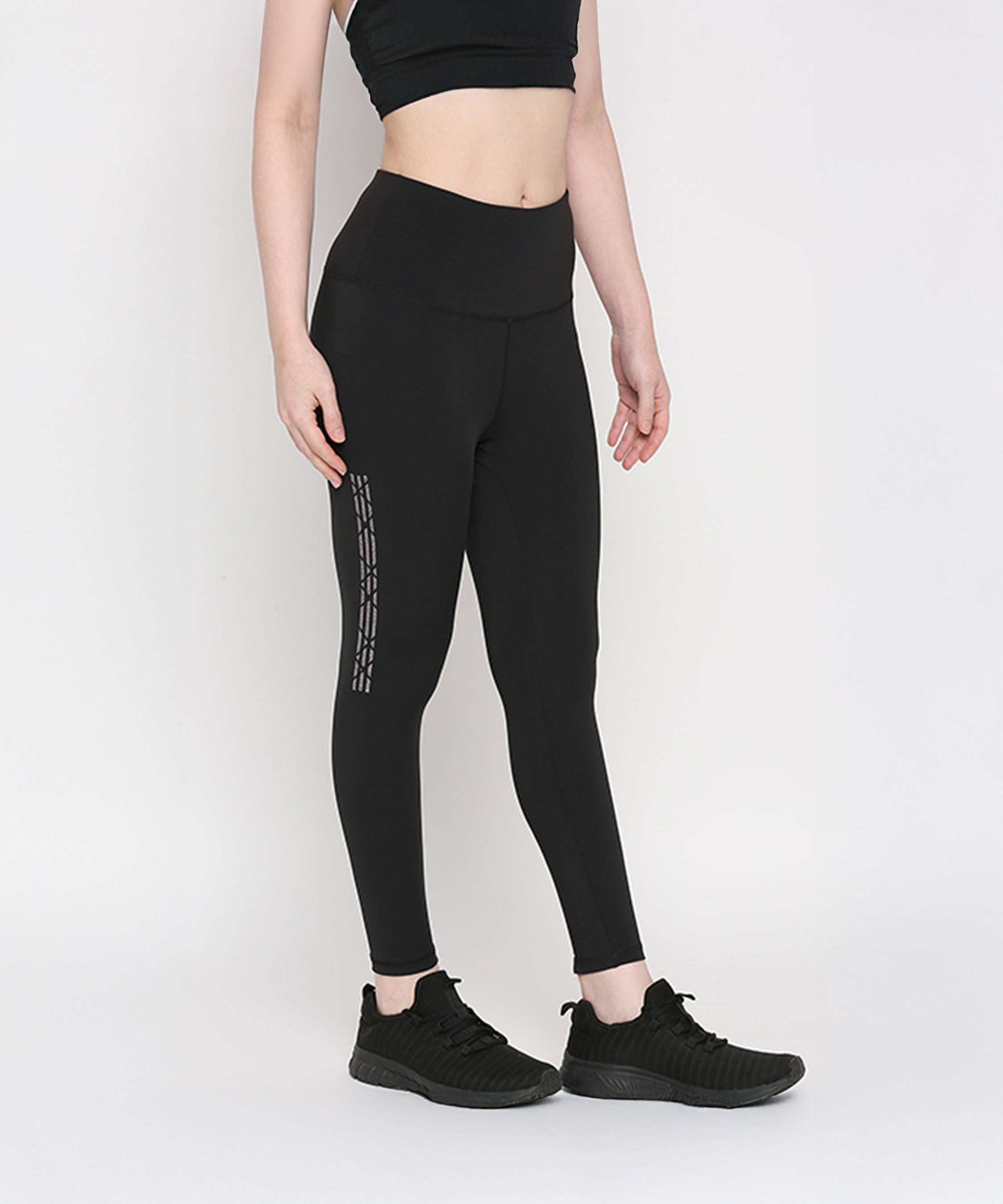Woman wearing Tuna Active Black Leggings With Print, paired with a black crop top and sneakers, stands against a white background, highlighting stylish women's gym wear.