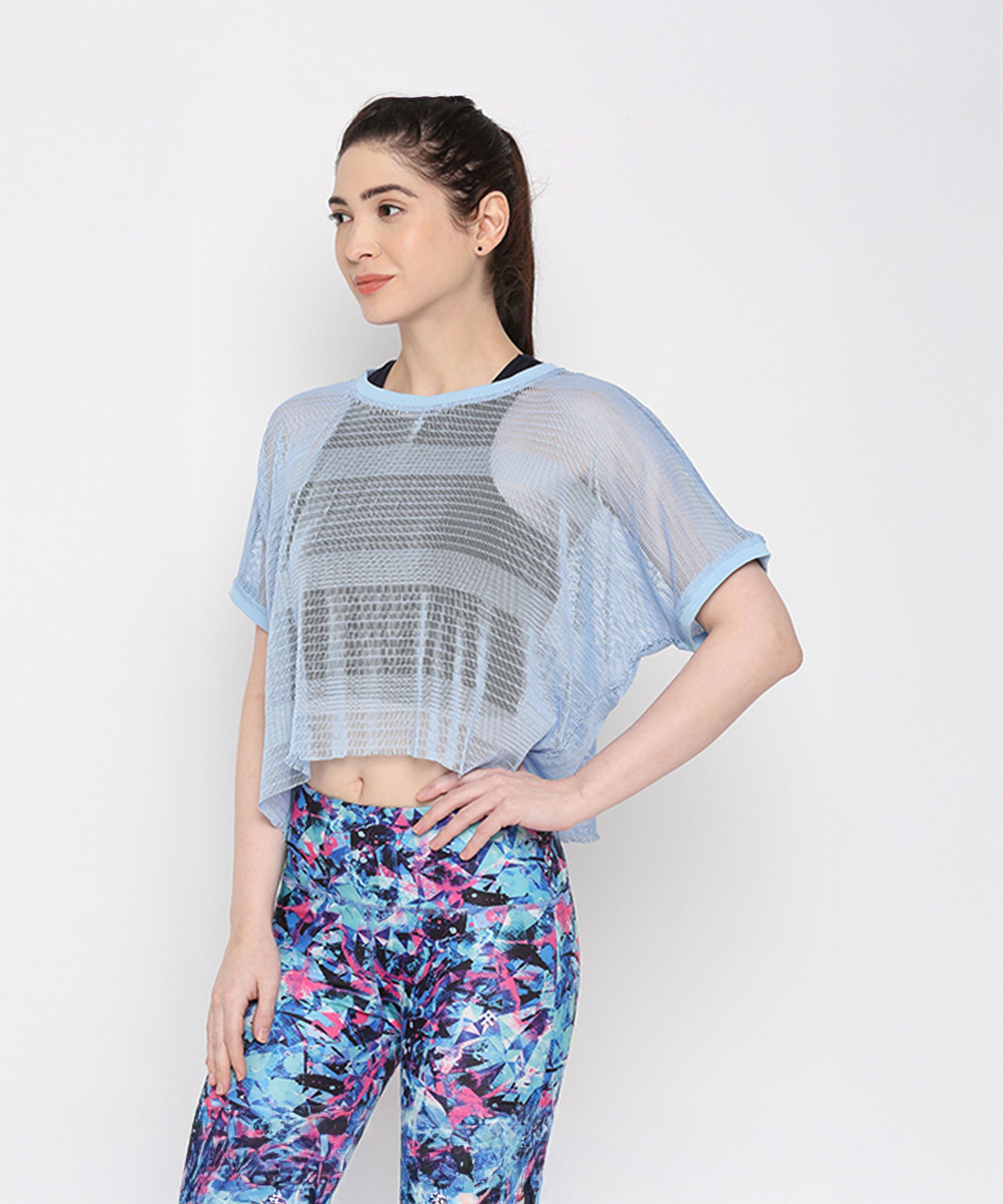 A woman showcases a sporty look in the Blue Netted Top and colorful floral leggings, posing against a plain white background.
