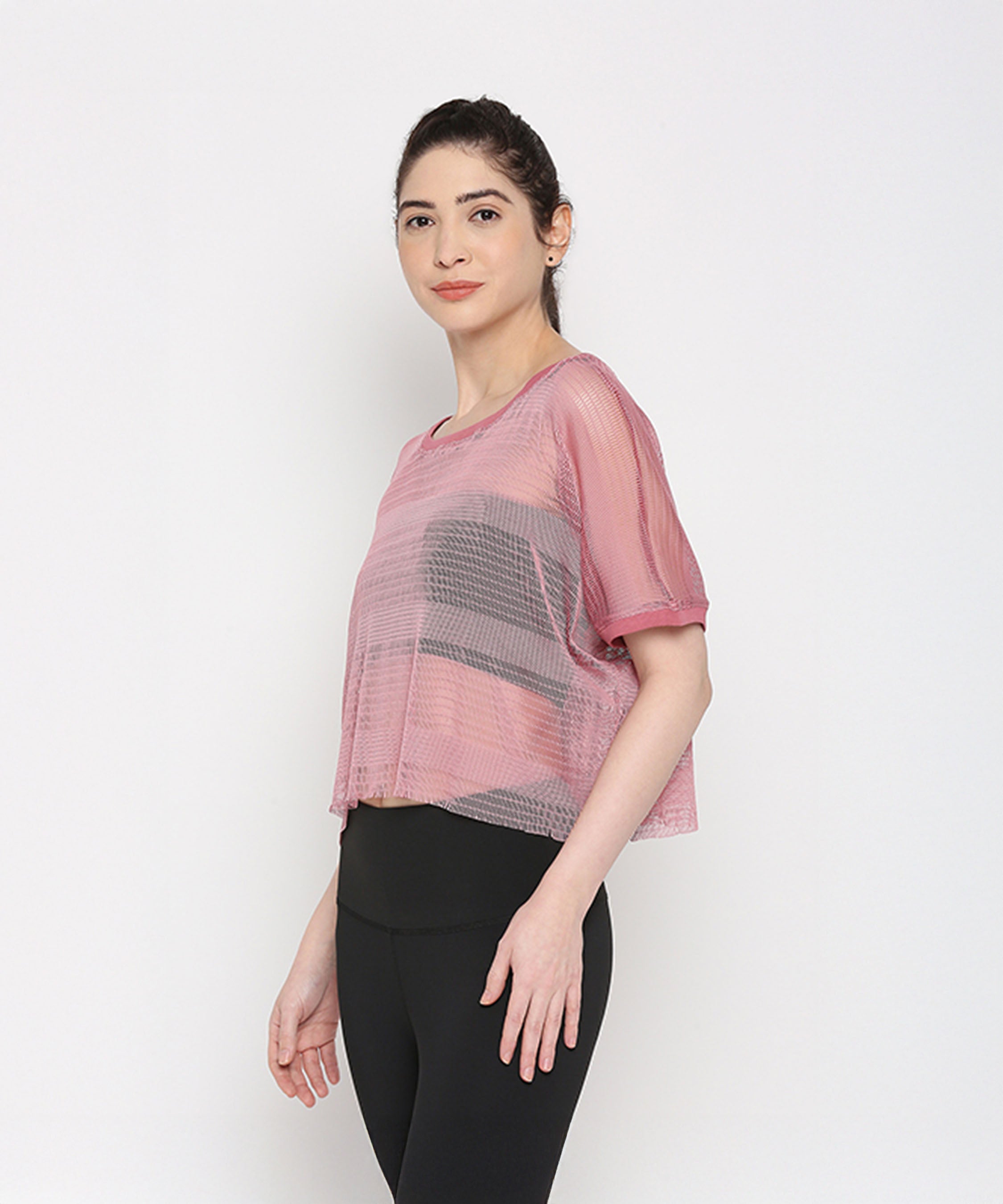 A woman models the Pink Netted Top with chic leggings, standing sideways against a plain white background to highlight her sporty style.