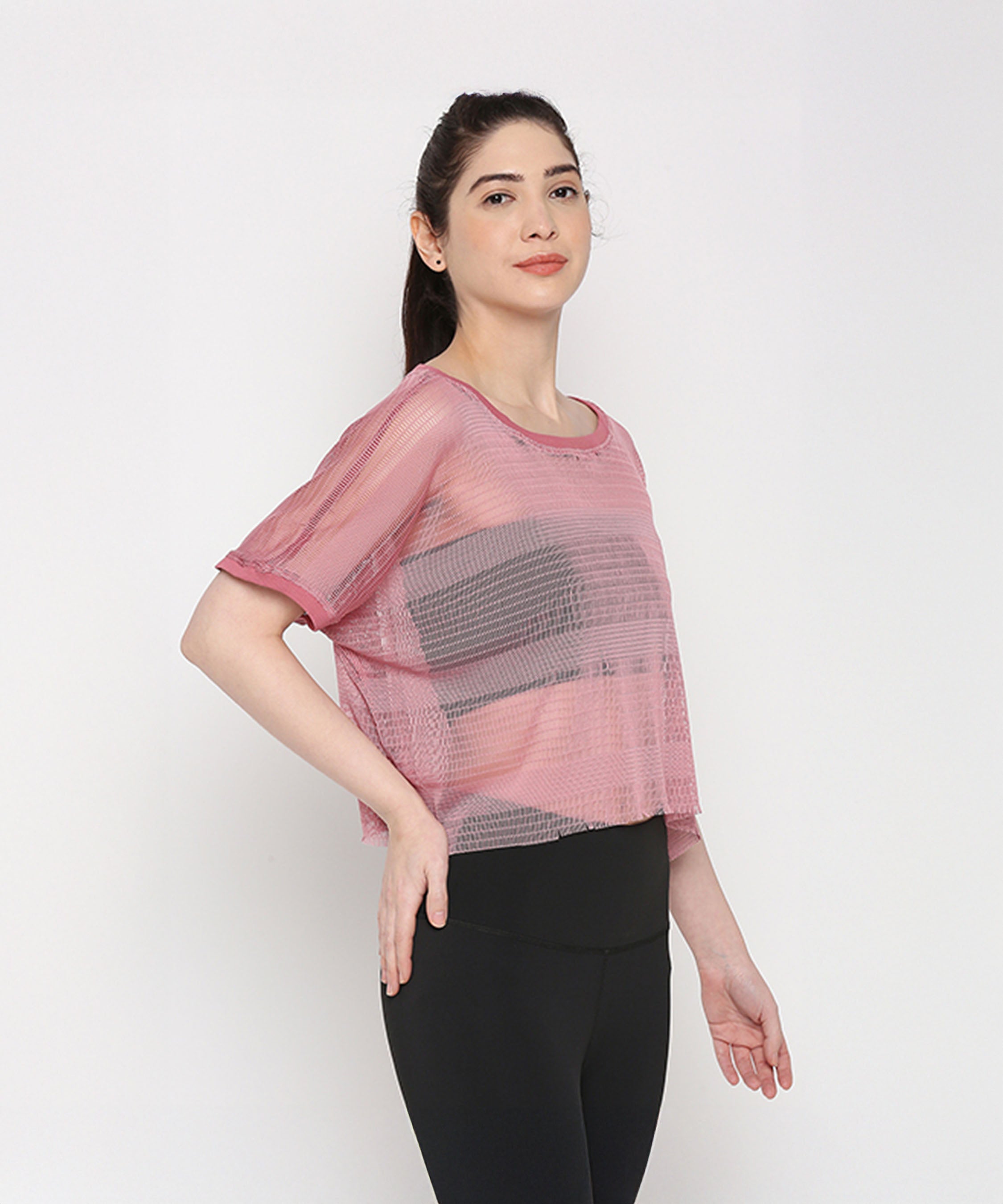 A woman models the Pink Netted Top with stylish leggings, striking a pose against a plain white background to showcase a sporty look.
