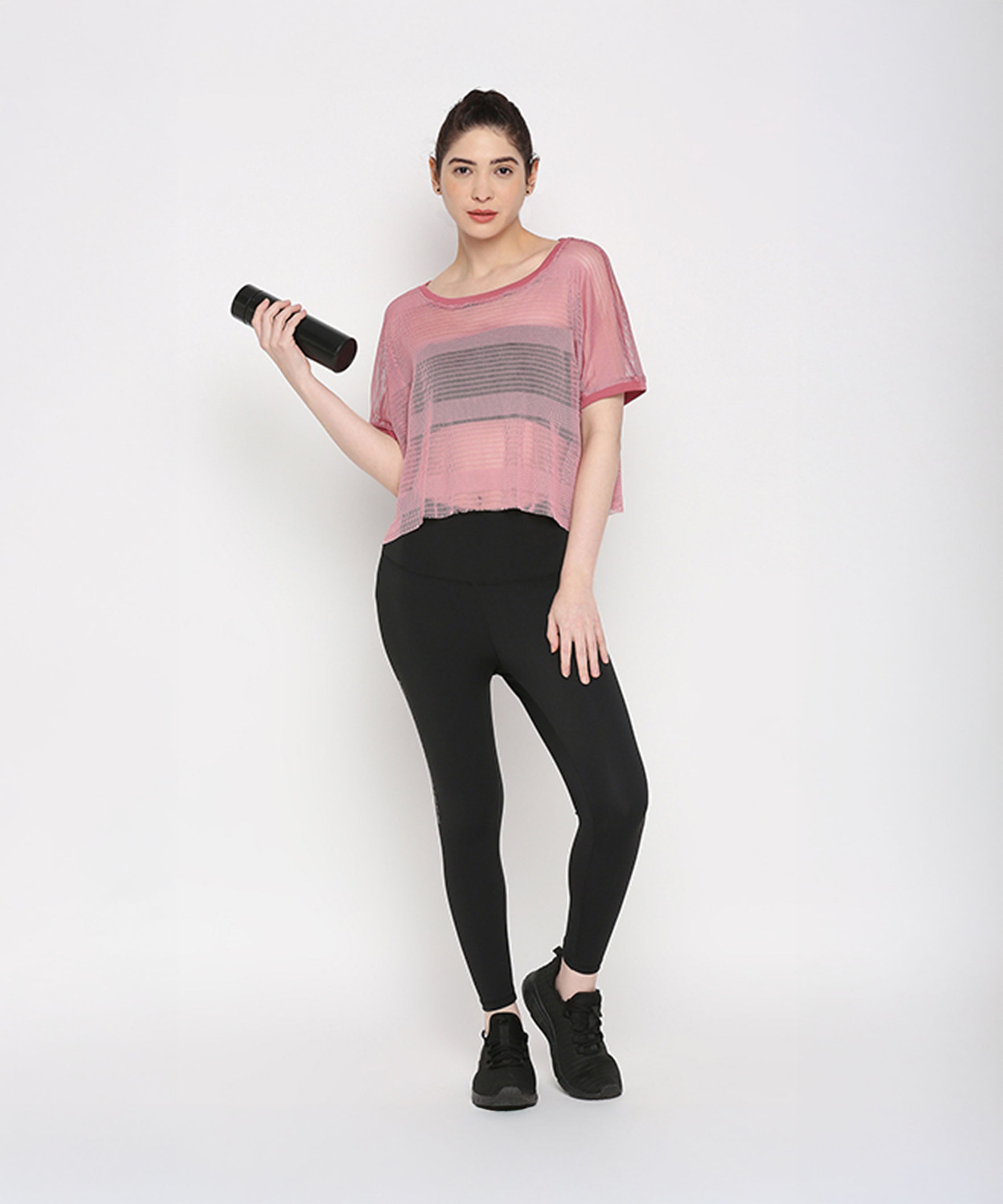 Woman wearing a Pink Netted Top and stylish leggings holds a water bottle, highlighting a sporty look against a plain white background.