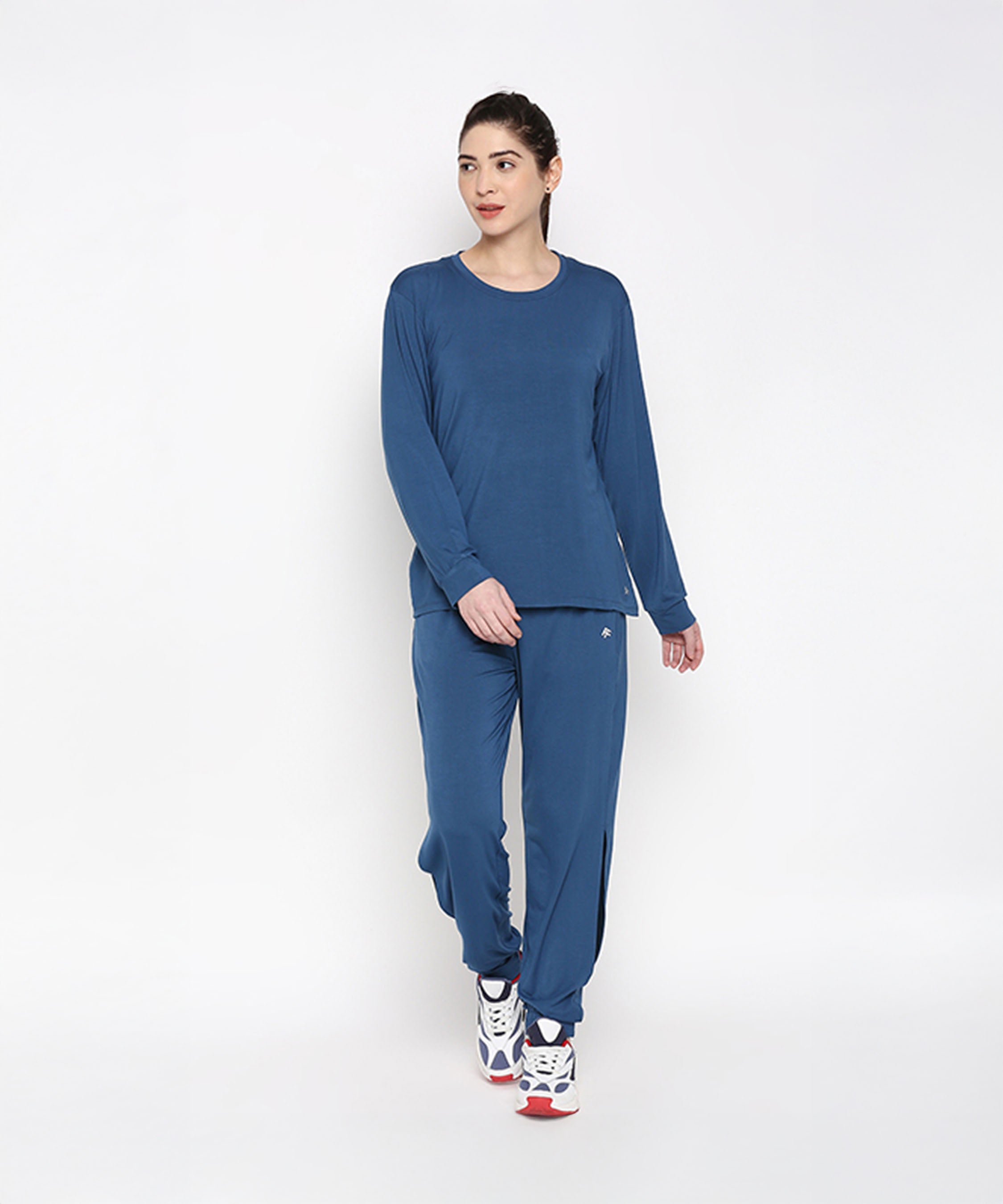 A woman wears the Atlantic Blue Active Duo, featuring a blue racerback top and cotton-modal joggers, styled with white athletic shoes against a plain background.