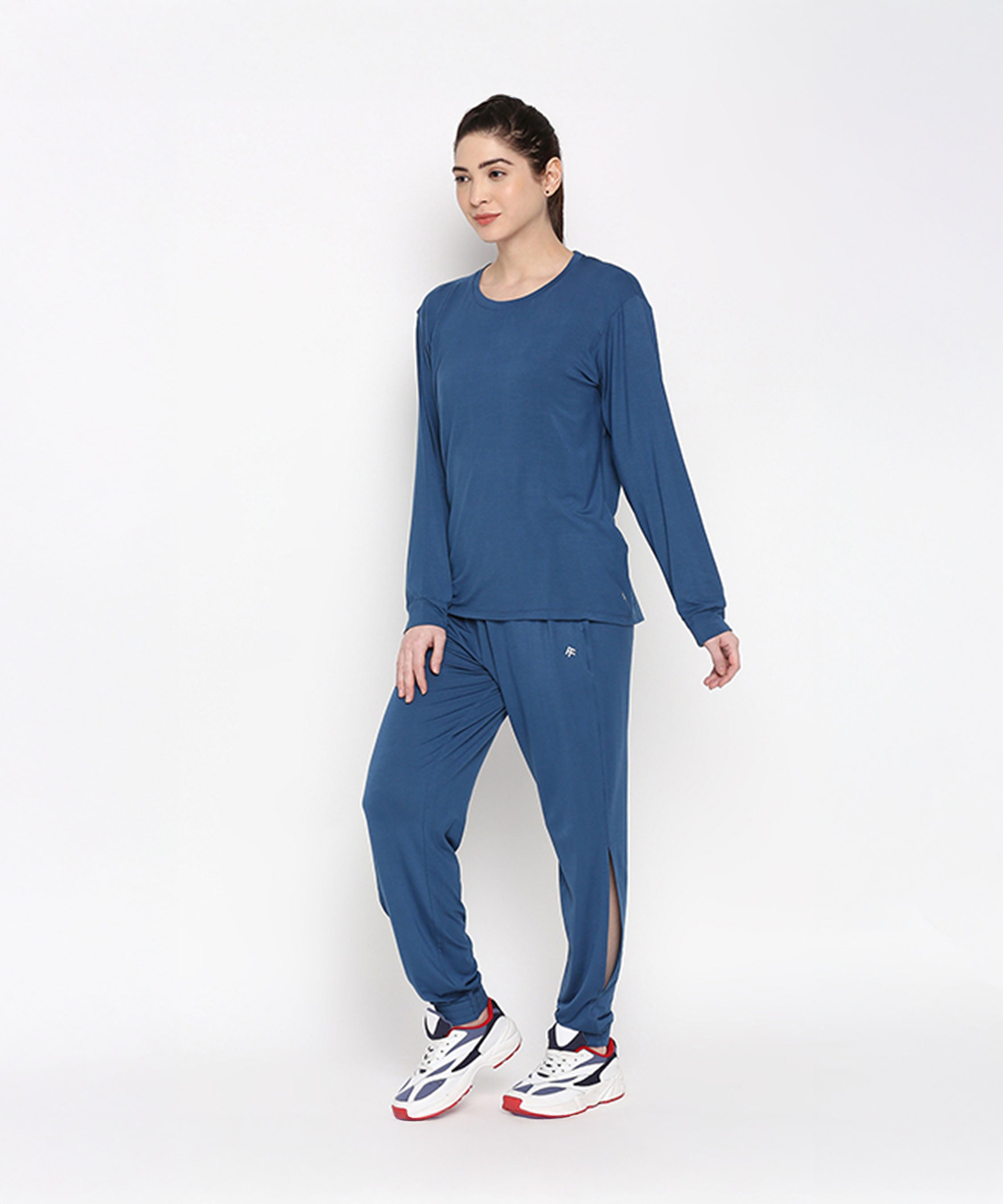 Woman wearing the Atlantic Blue Active Duo—racerback top and joggers made from buttery soft fabric—paired with white sneakers, stands against a plain background.