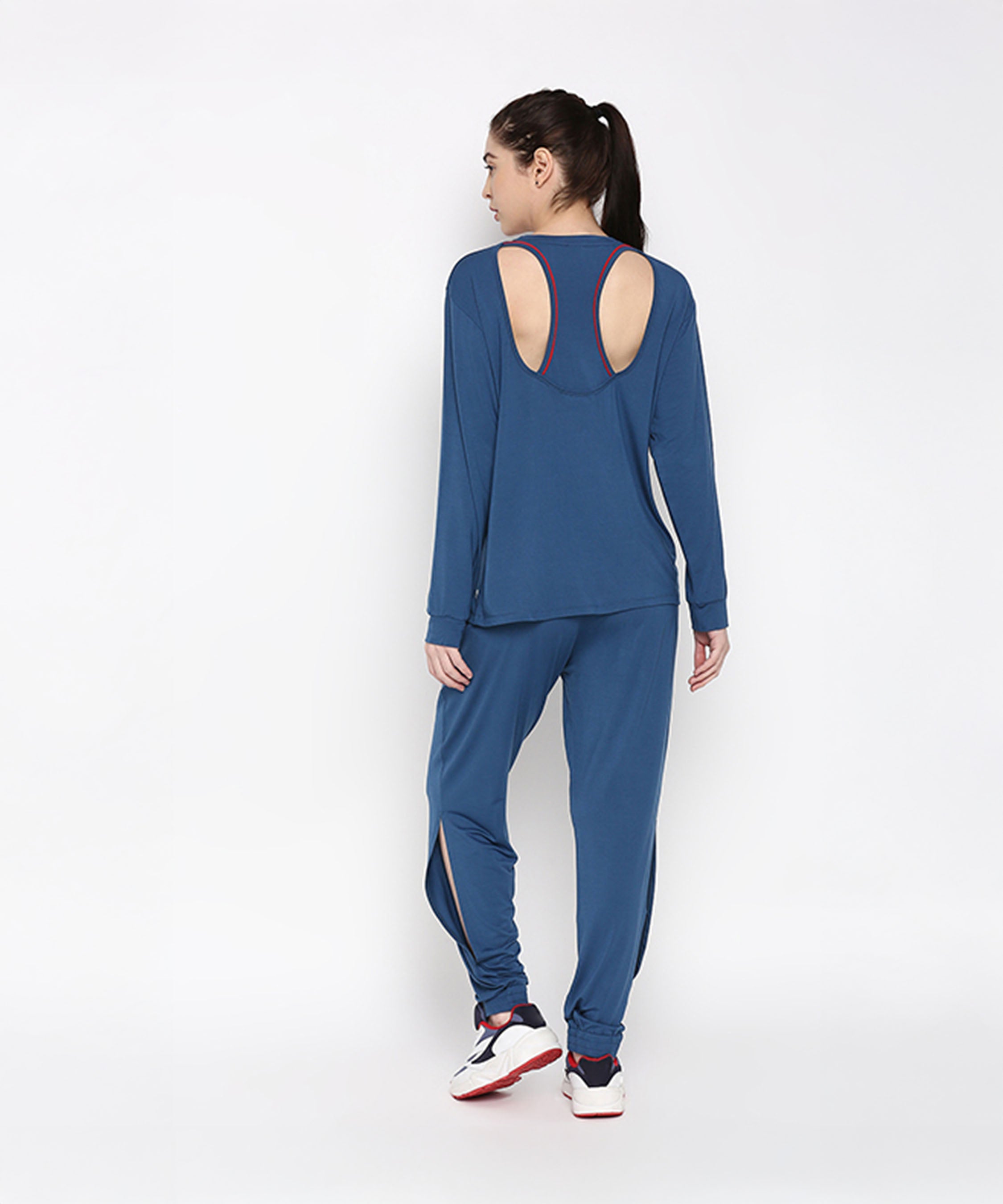 Woman in Atlantic Blue Active Duo—blue racerback top crafted from buttery soft fabric and cotton modal joggers—sporting a ponytail and white sneakers, facing away.