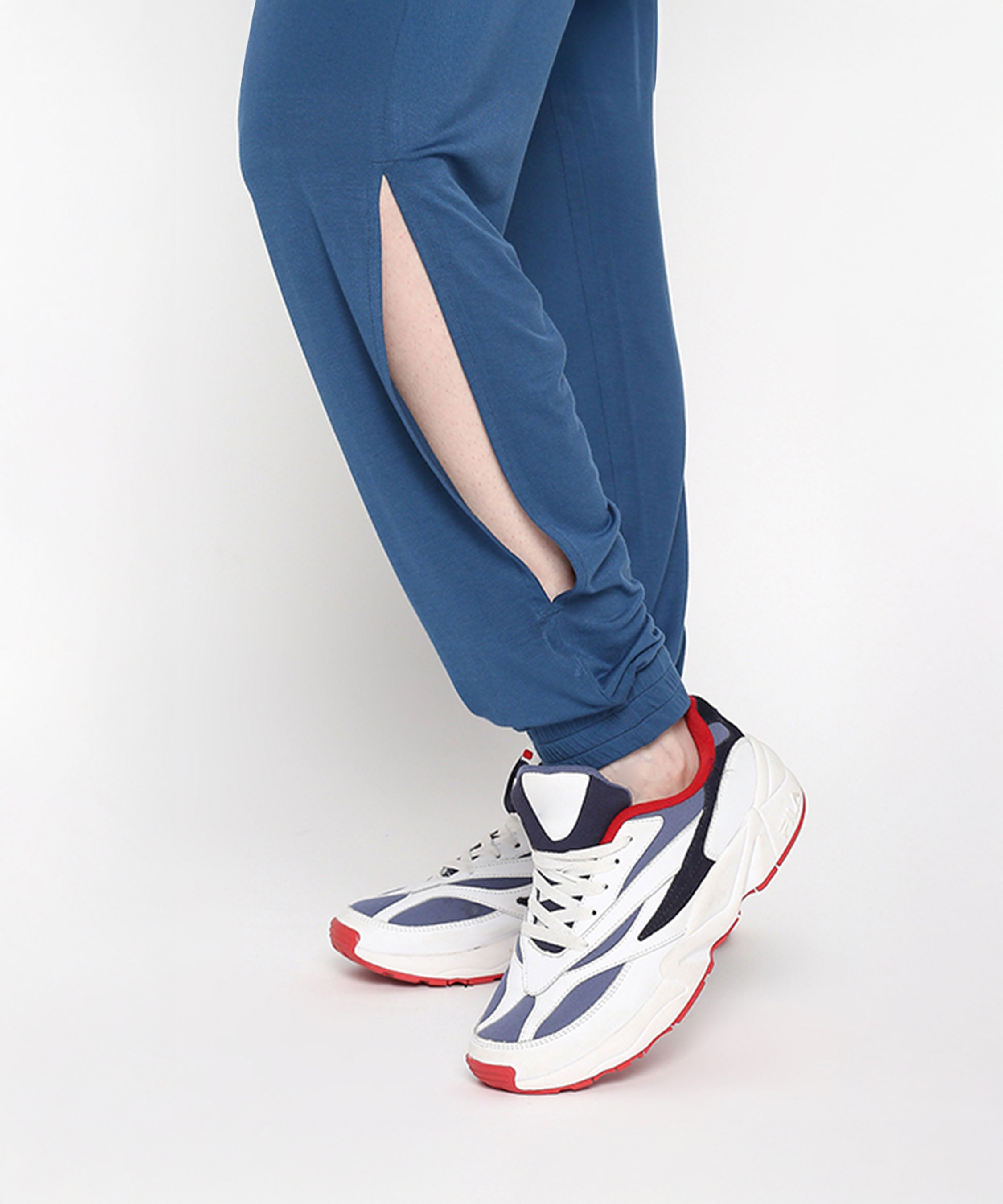 Wearing the Atlantic Blue Active Duo pants, known for their buttery soft fabric and side slit, styled with white sneakers featuring navy and red accents while standing on tiptoe.