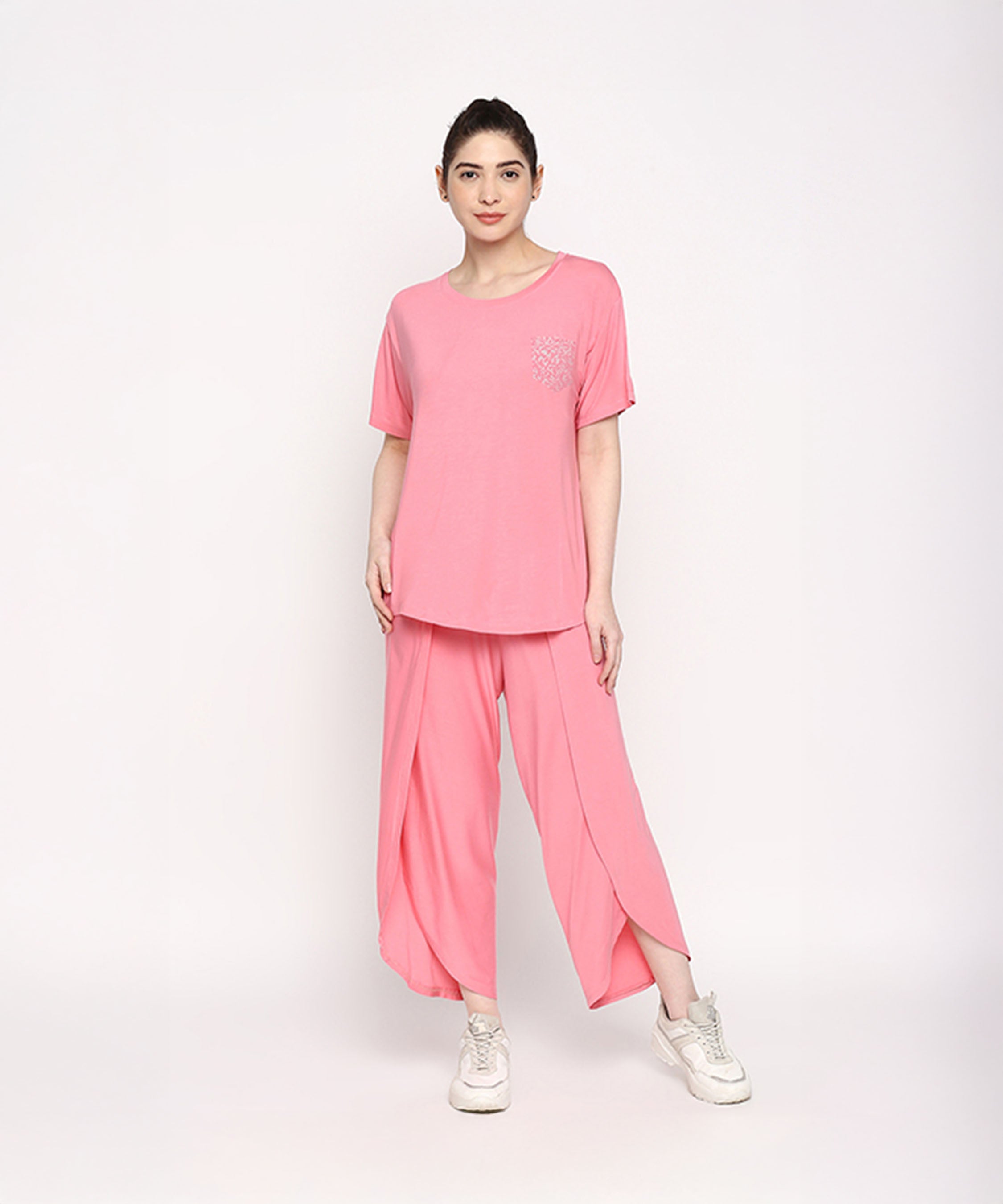 A woman stands against a plain white background wearing the Coral Blissful Tulip Set, featuring a coral pink Cotton Modal top and matching tulip pants.