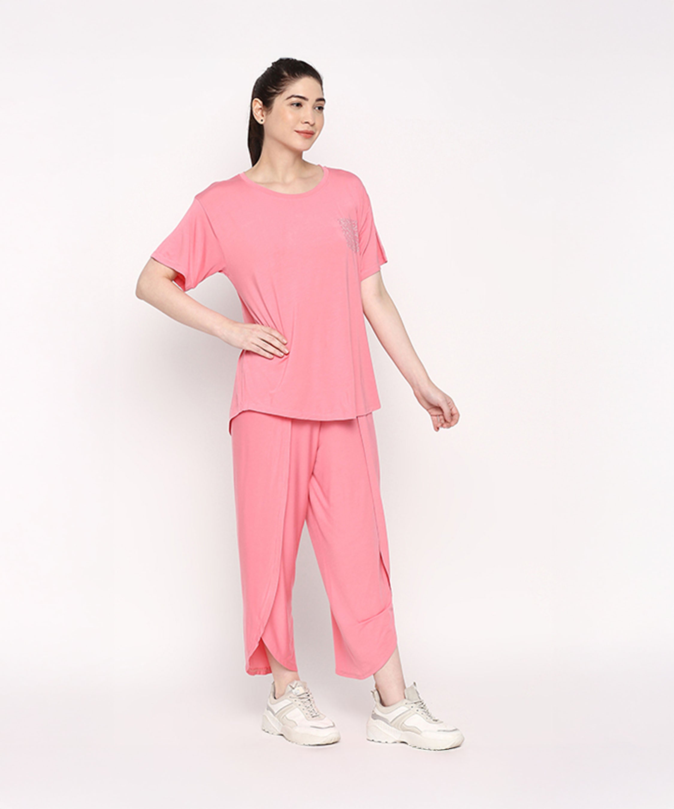 Woman wearing the Coral Blissful Tulip Set—a coral pink cotton modal loungewear outfit with a tulip pant—paired with white sneakers, posing against a plain white background.