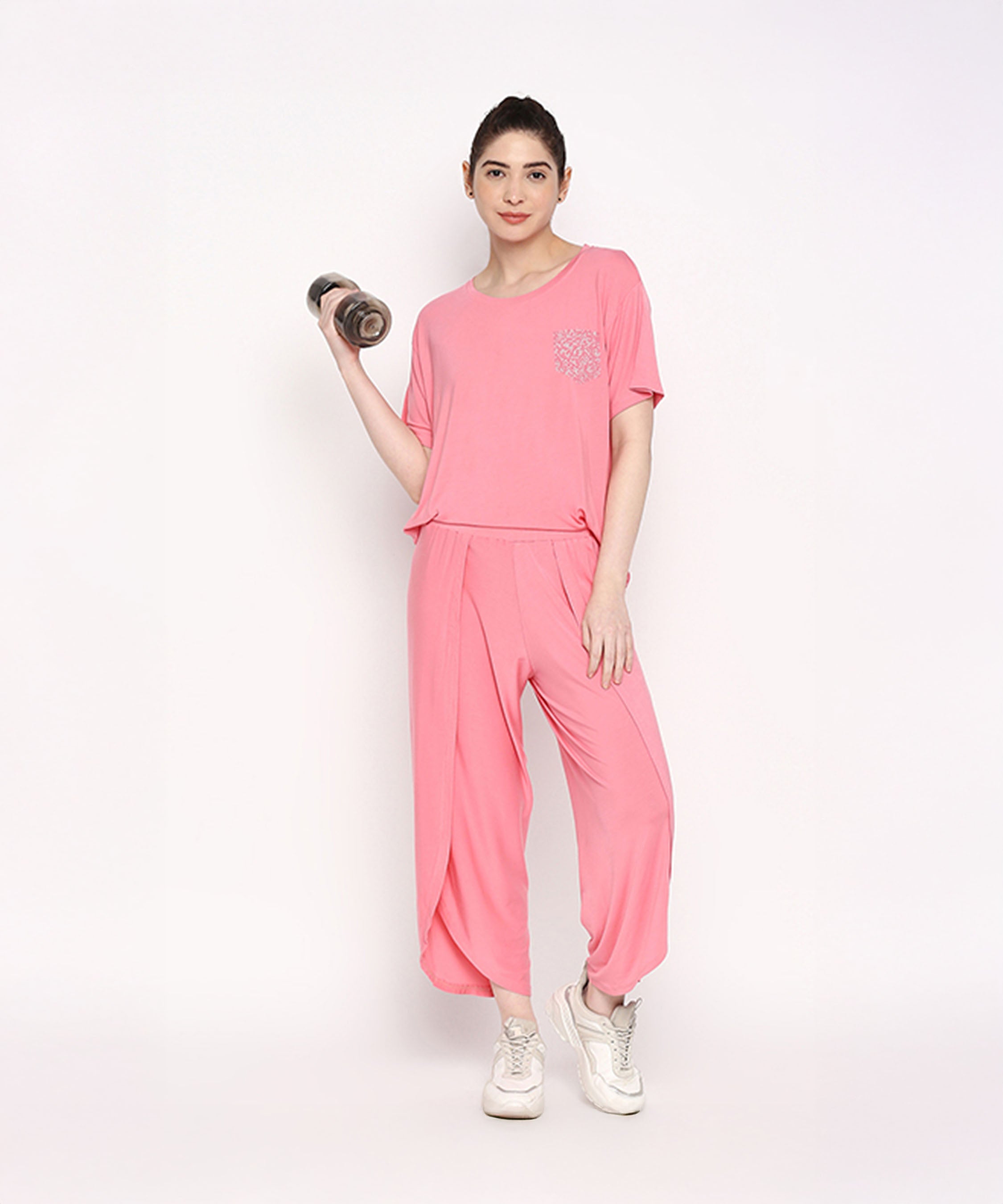 Woman wearing the Coral Blissful Tulip Set, made from Cotton Modal, balances on one leg and holds a dumbbell against a plain white background.