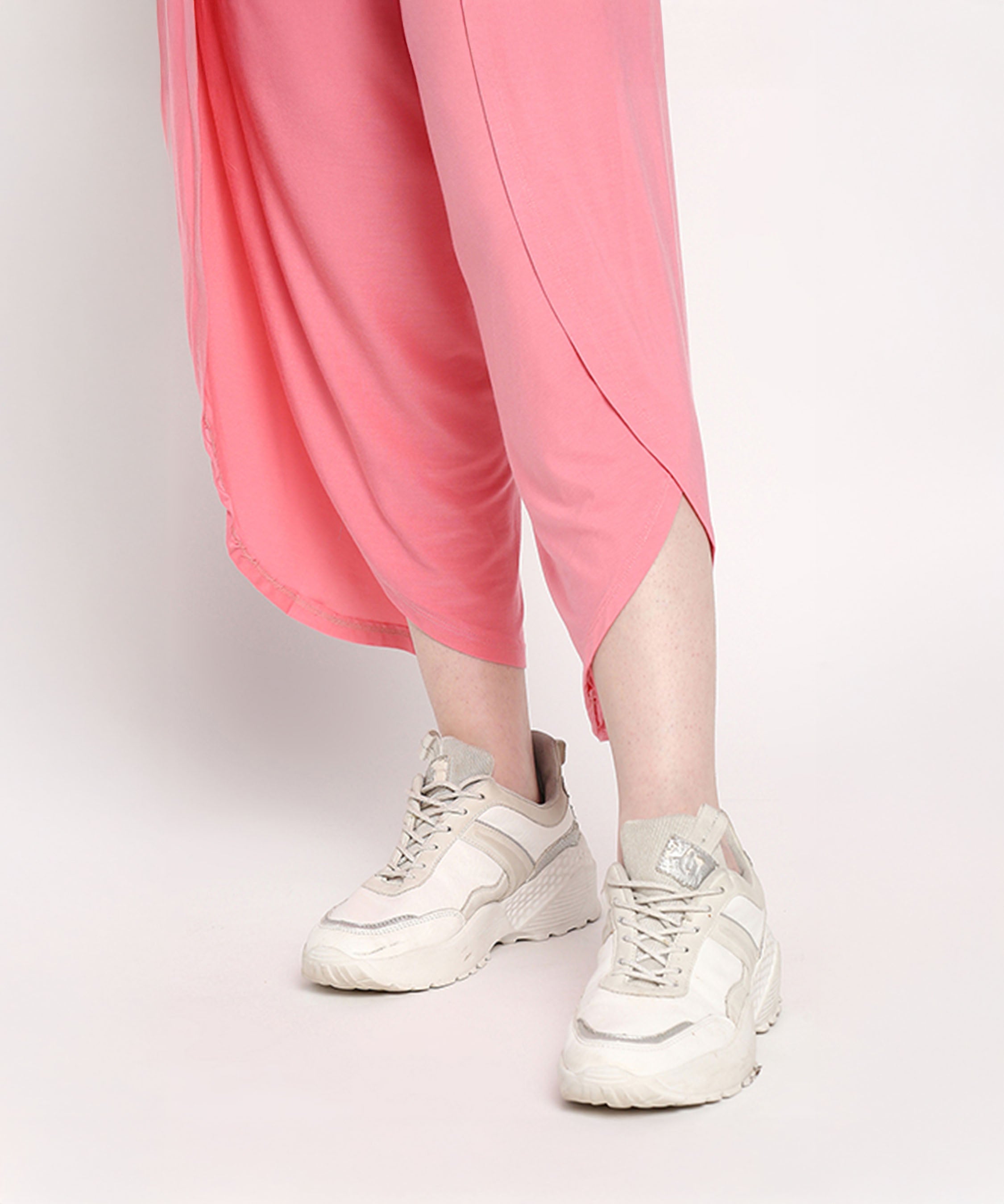 A person models the Coral Blissful Tulip Set—featuring a coral pink top and light pink cotton modal tulip pants—with white sneakers against a light background.