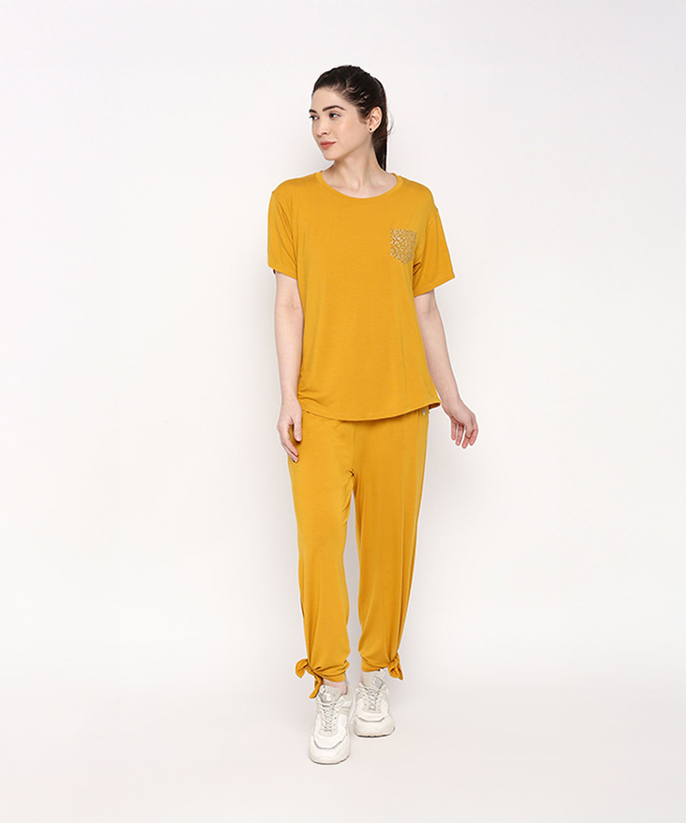 A woman wears the Mustard Chic Set—mustard yellow top and cotton modal trackpant pajama with soft elasticated waistband—paired with white sneakers, standing against a plain white background.