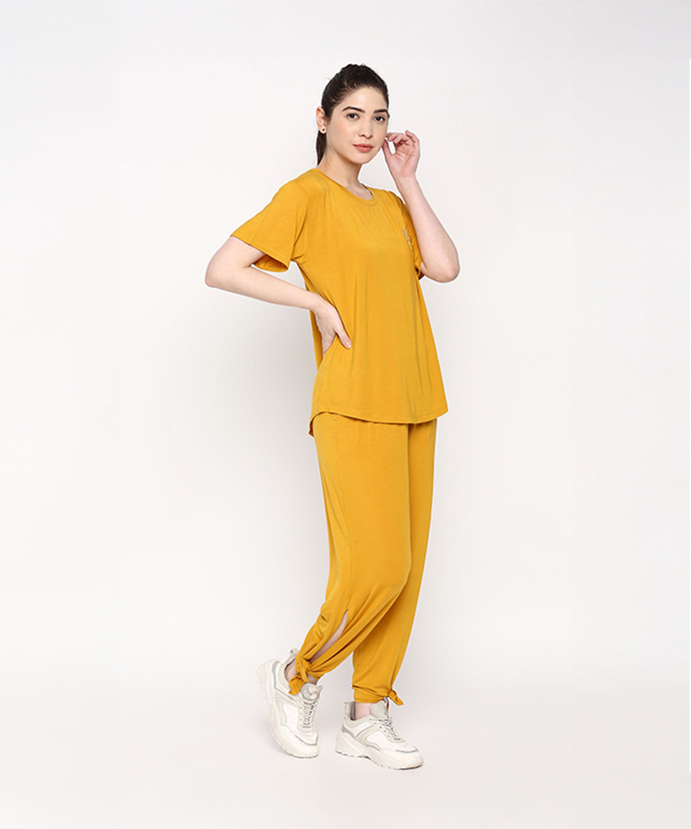 Woman in the Mustard Chic Set, featuring a mustard yellow top and Cotton Modal Trackpant with a soft elasticated waistband, pairs the look with white sneakers against a plain white background.