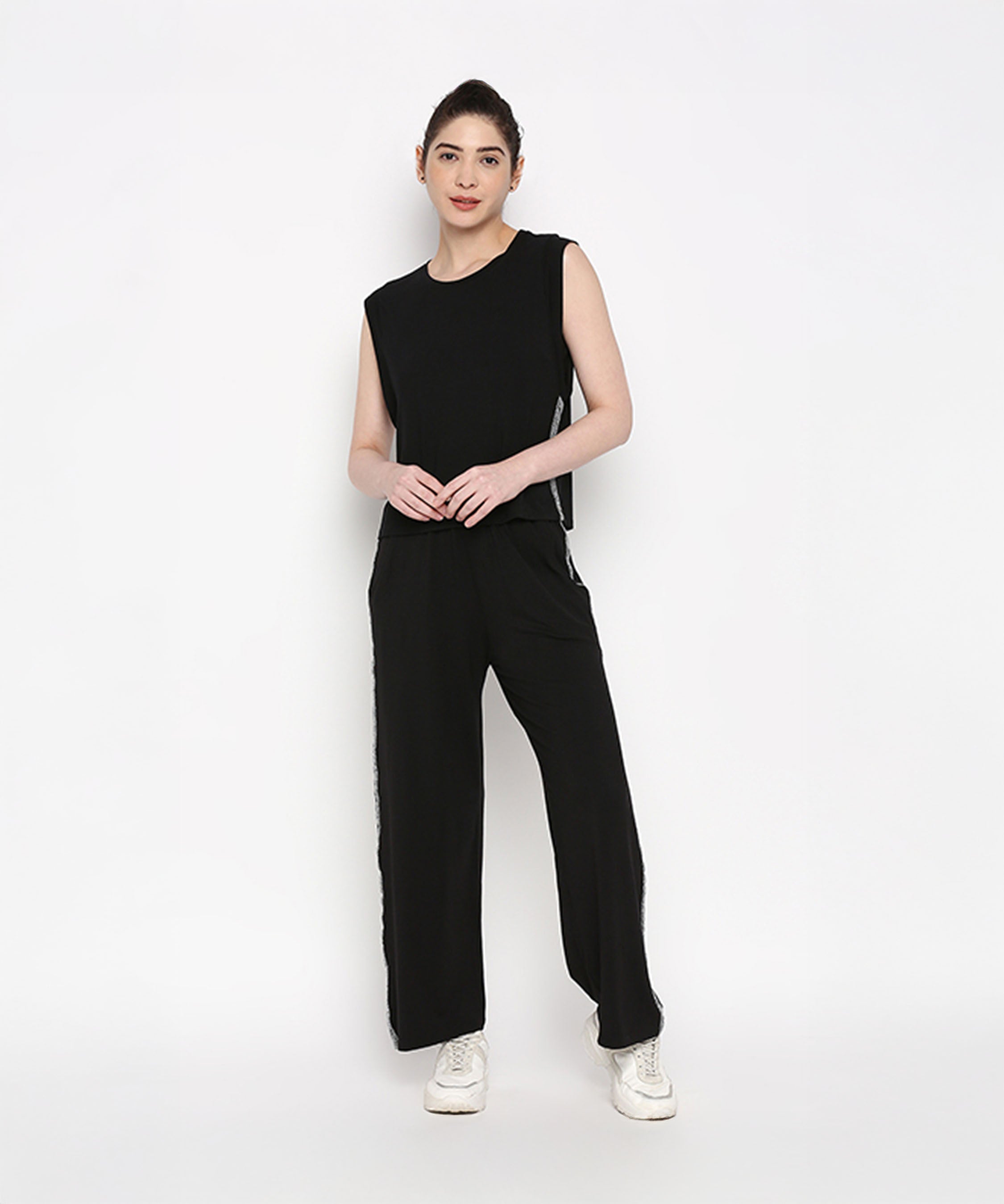 A woman stands smiling in the Comfy Black Set with Side Sparkle—featuring a sleeveless black top and loose fit track pants with glitter patches—crafted from soft cotton lycra, against a plain white background.