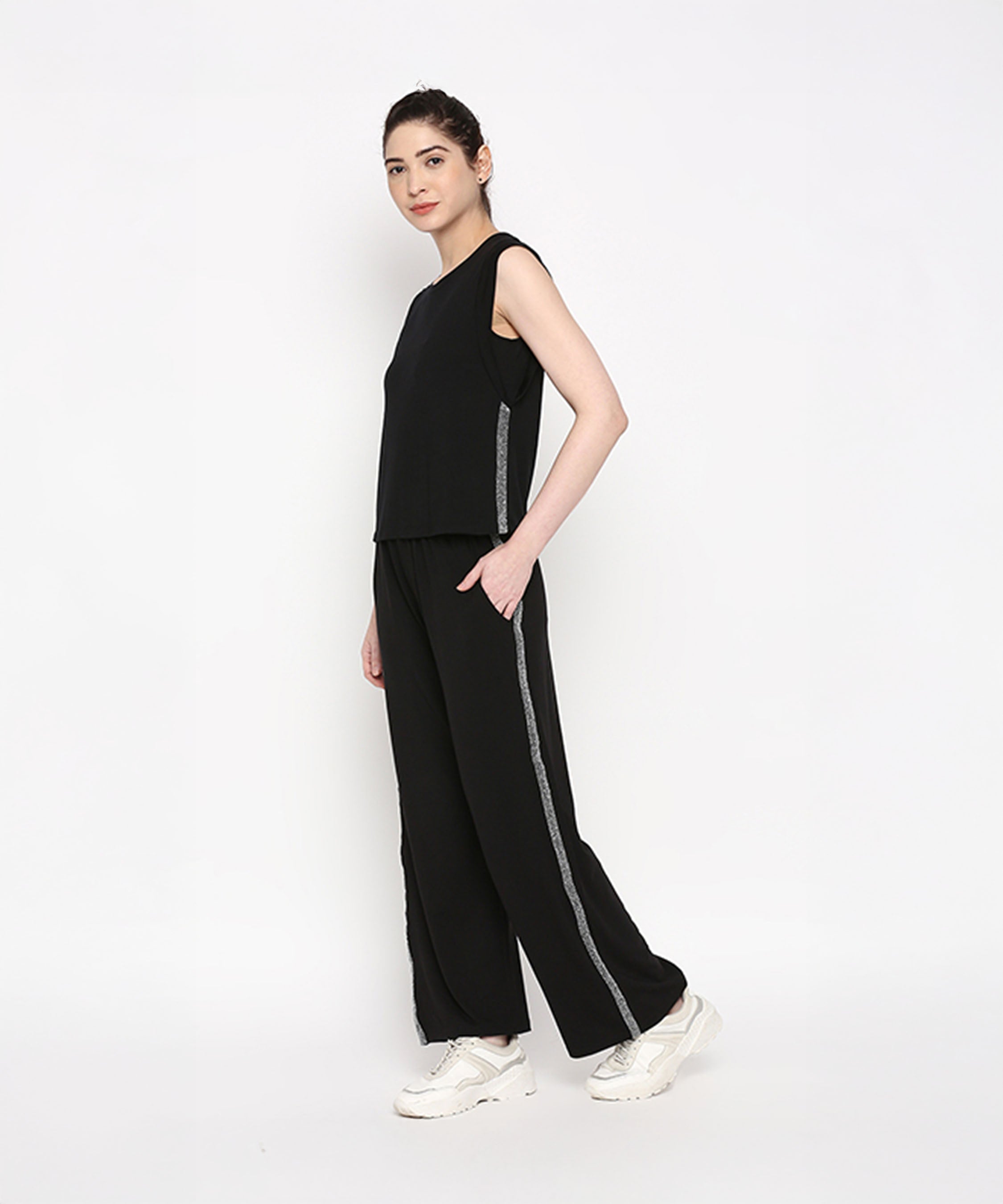 Woman wearing the Comfy Black Set with Side Sparkle, a black sleeveless top and loose fit track pant featuring side stripes, crafted from comfortable cotton lycra, standing against a white background.